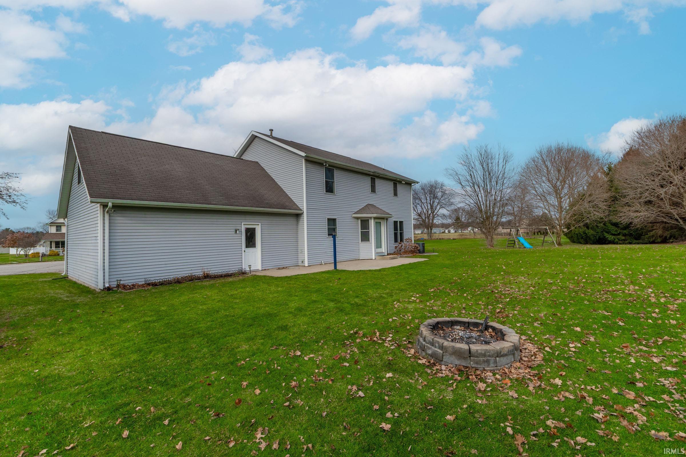 Rear view of property with a yard, a fire pit, a playground, a patio area, and a shingled roof
