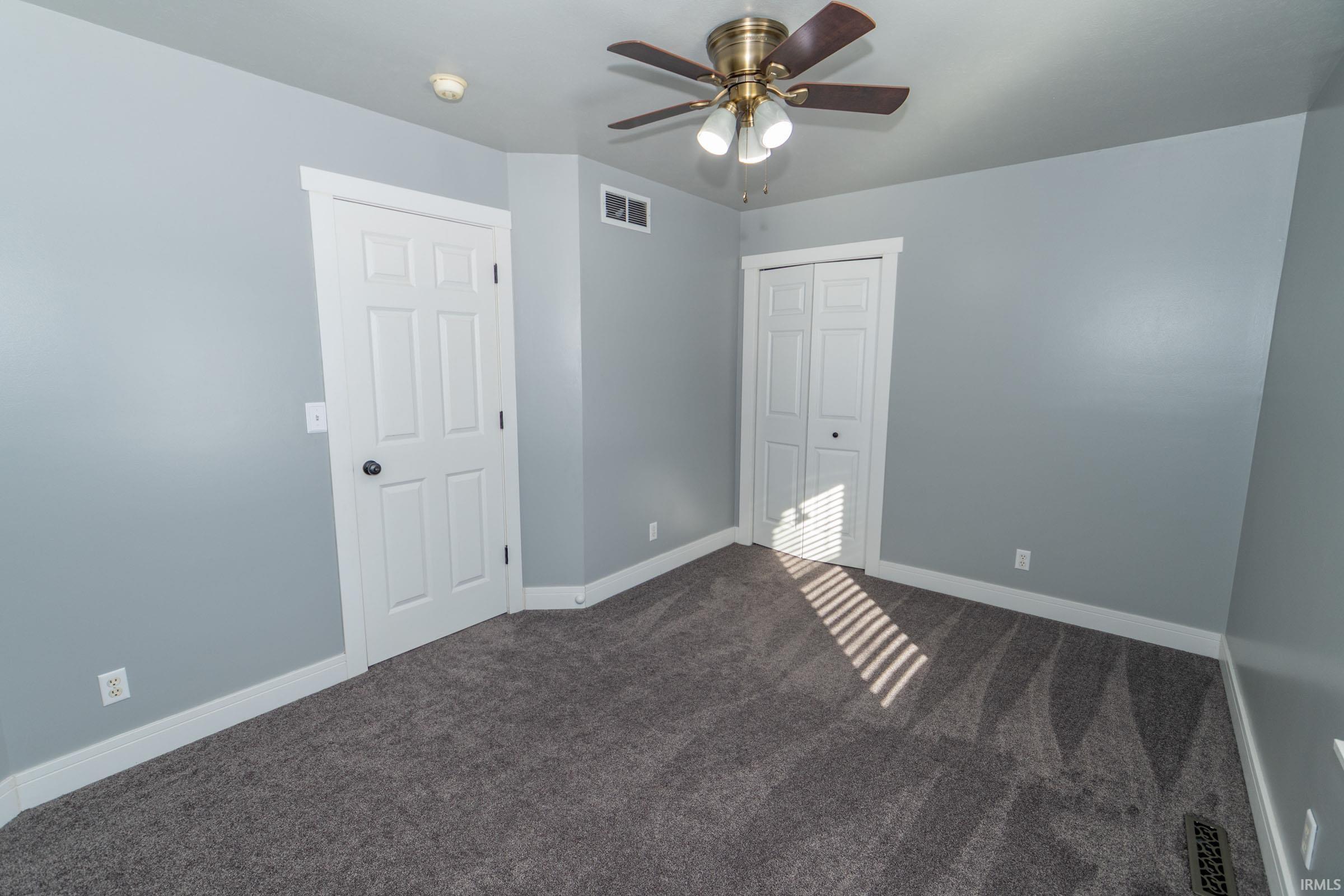 Unfurnished bedroom with a closet, dark carpet, and ceiling fan