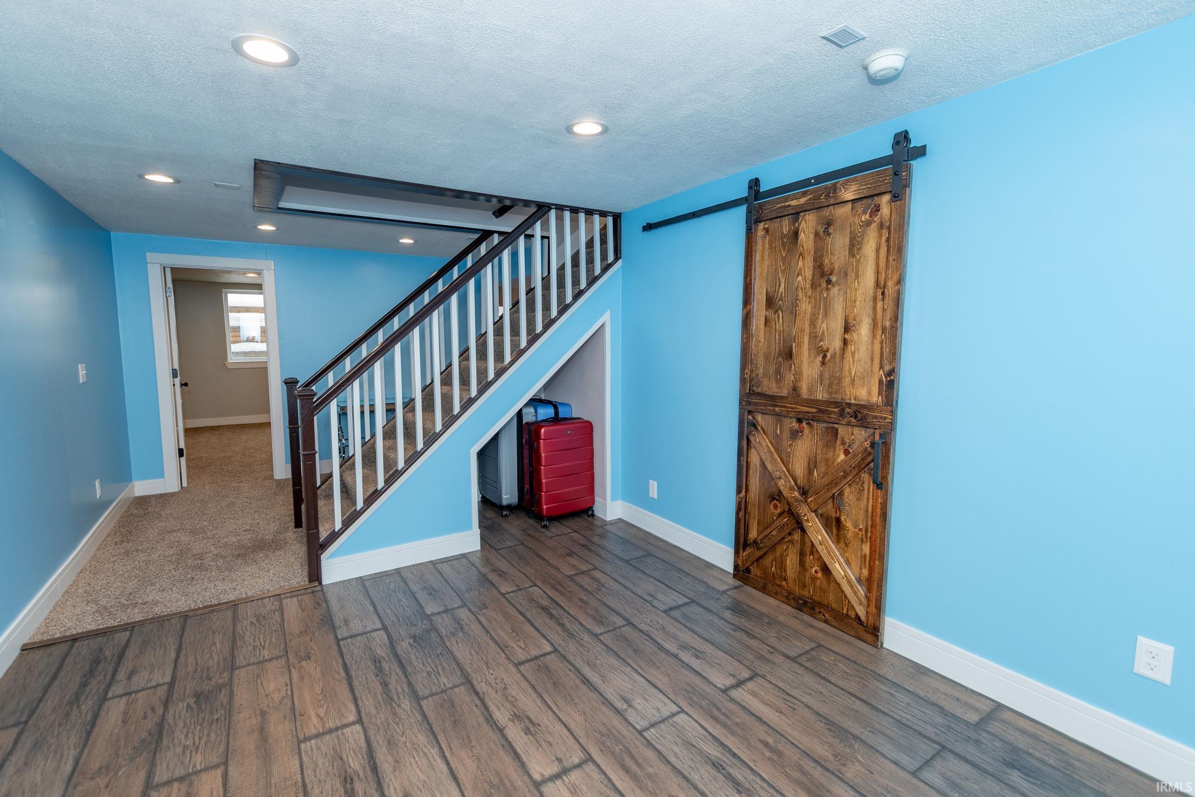Unfurnished living room with a barn door, wood finished floors, a textured ceiling, stairs, and recessed lighting