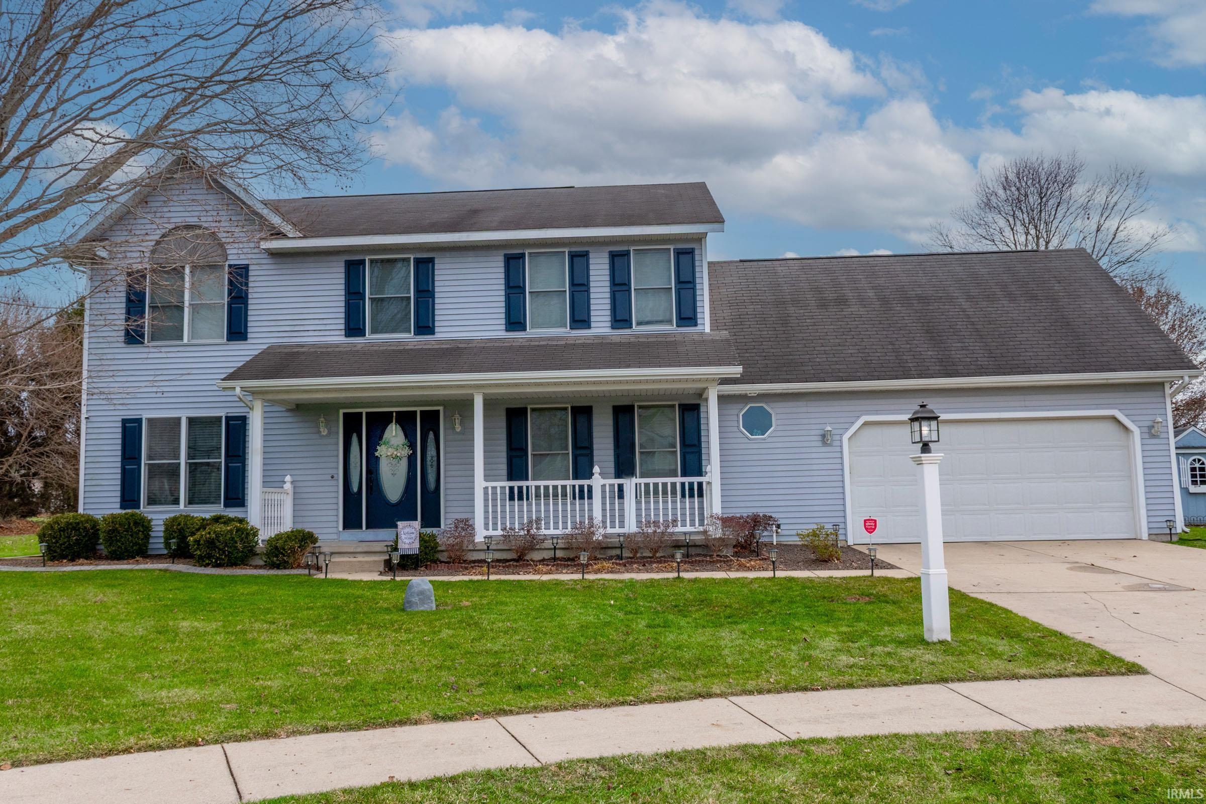 Traditional home with covered porch, a front lawn, driveway, and an attached garage