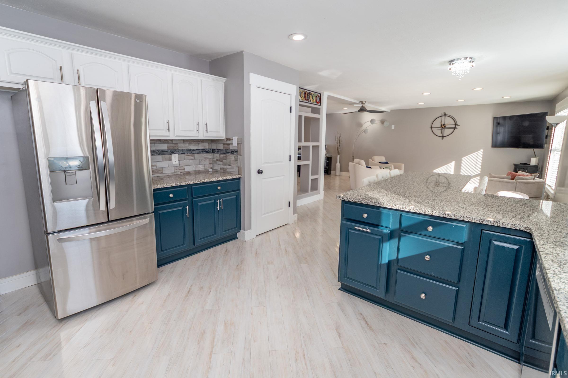 Kitchen with stainless steel fridge with ice dispenser, light stone counters, open floor plan, blue cabinets, and a ceiling fan
