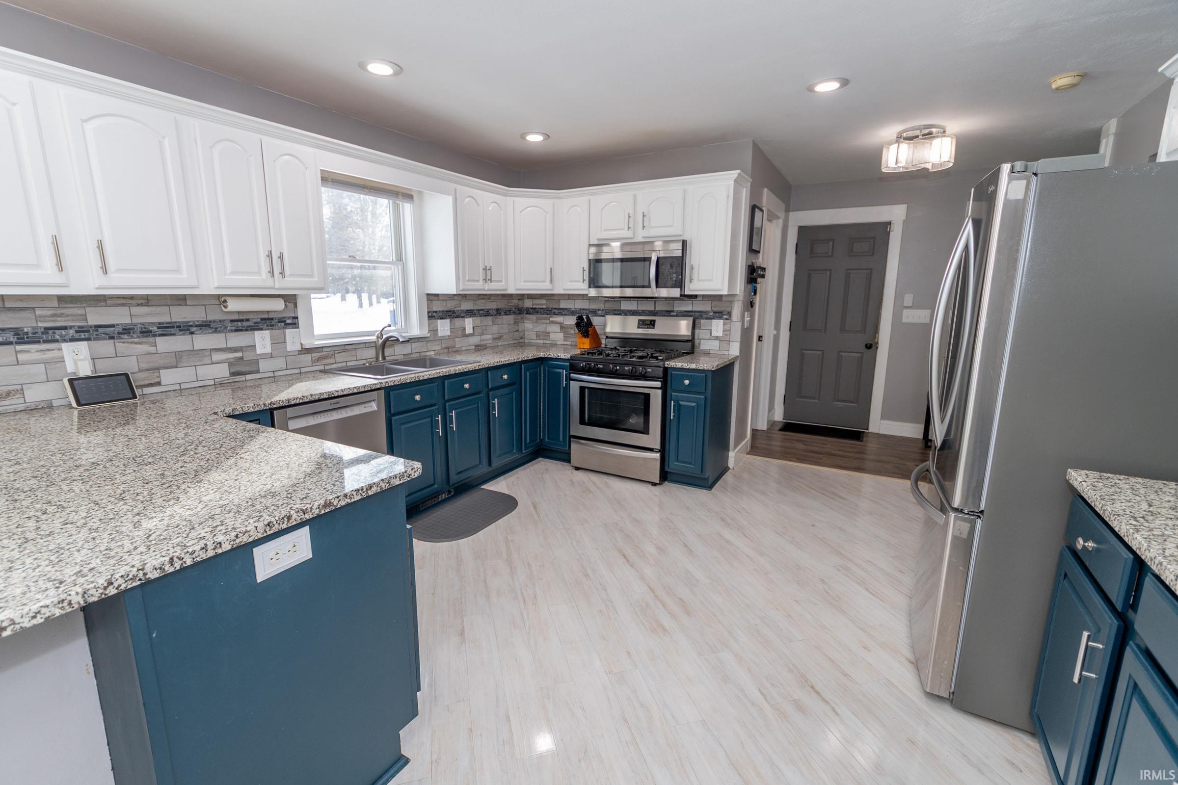 Kitchen with blue cabinets, stainless steel appliances, light stone countertops, white cabinets, and recessed lighting