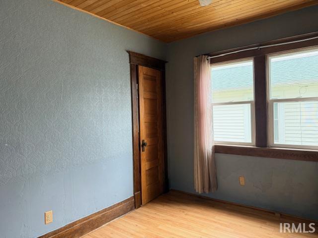 Empty room featuring light wood-style floors, wood ceiling, and a textured wall
