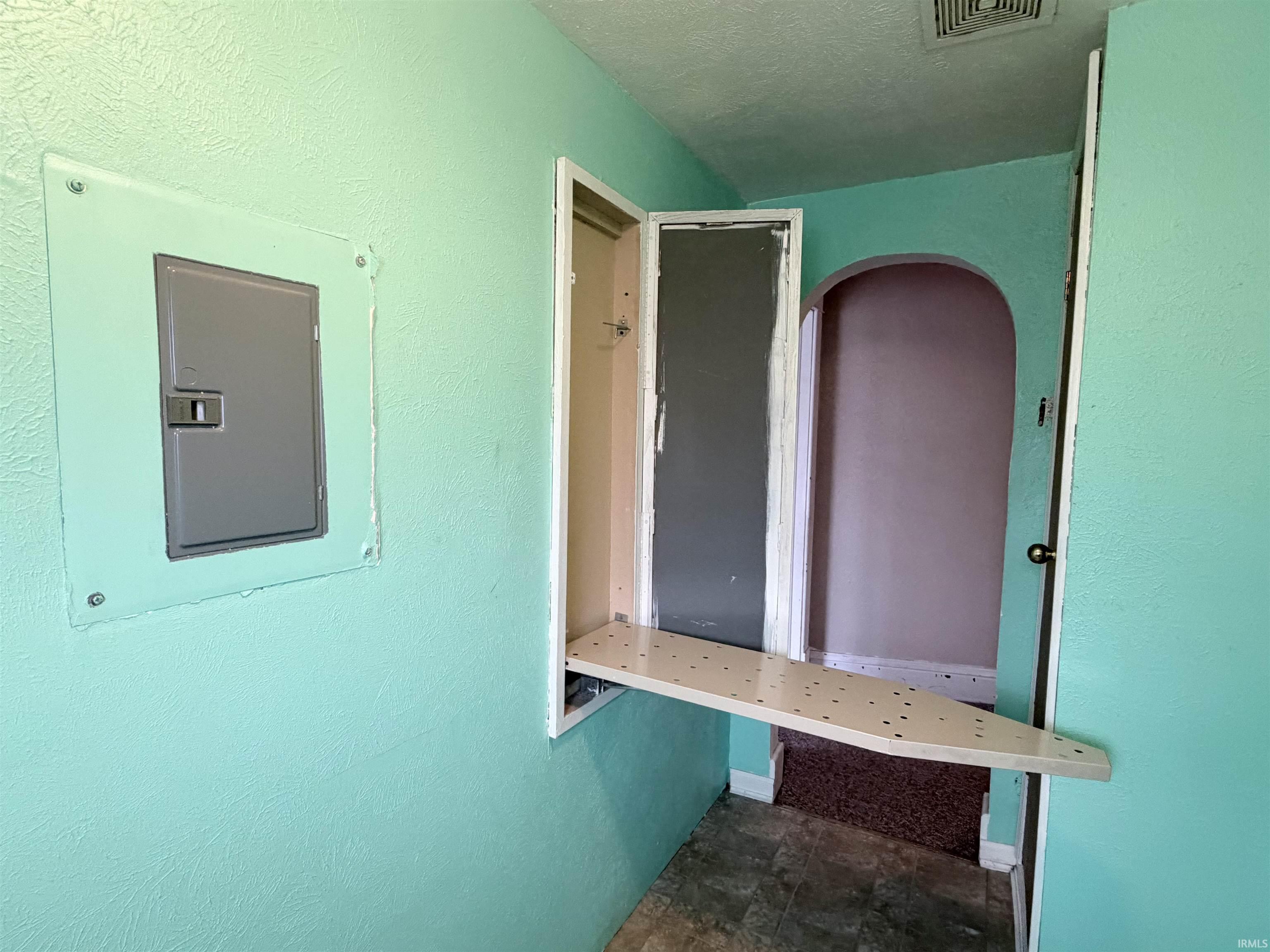 Unfurnished office with electric panel, stone finish flooring, a textured ceiling, and a textured wall