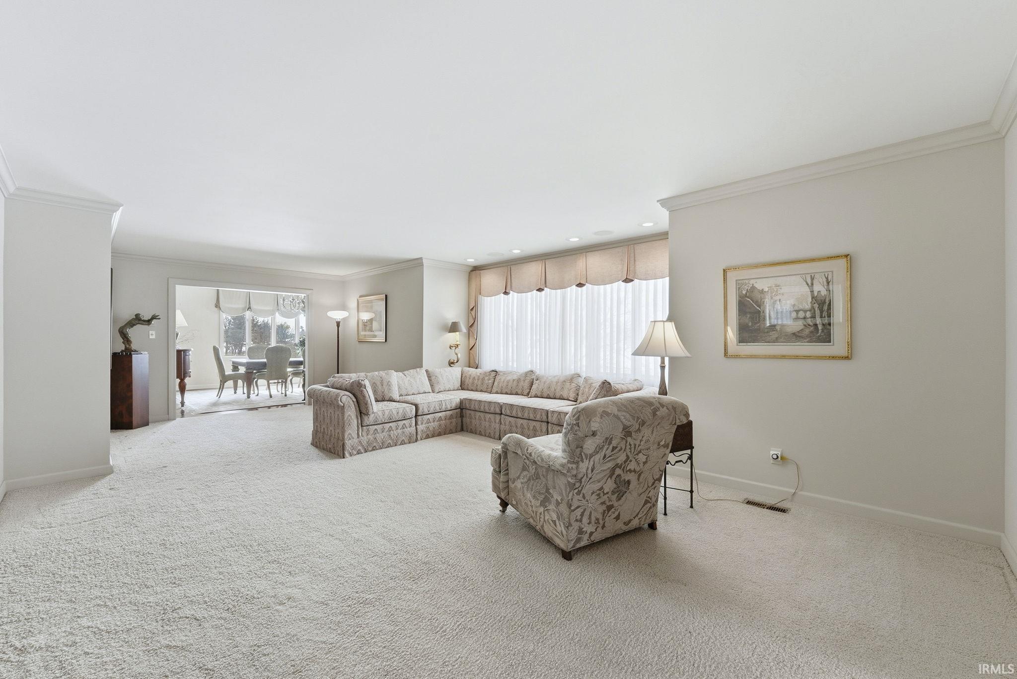Carpeted living area with ornamental molding and healthy amount of natural light