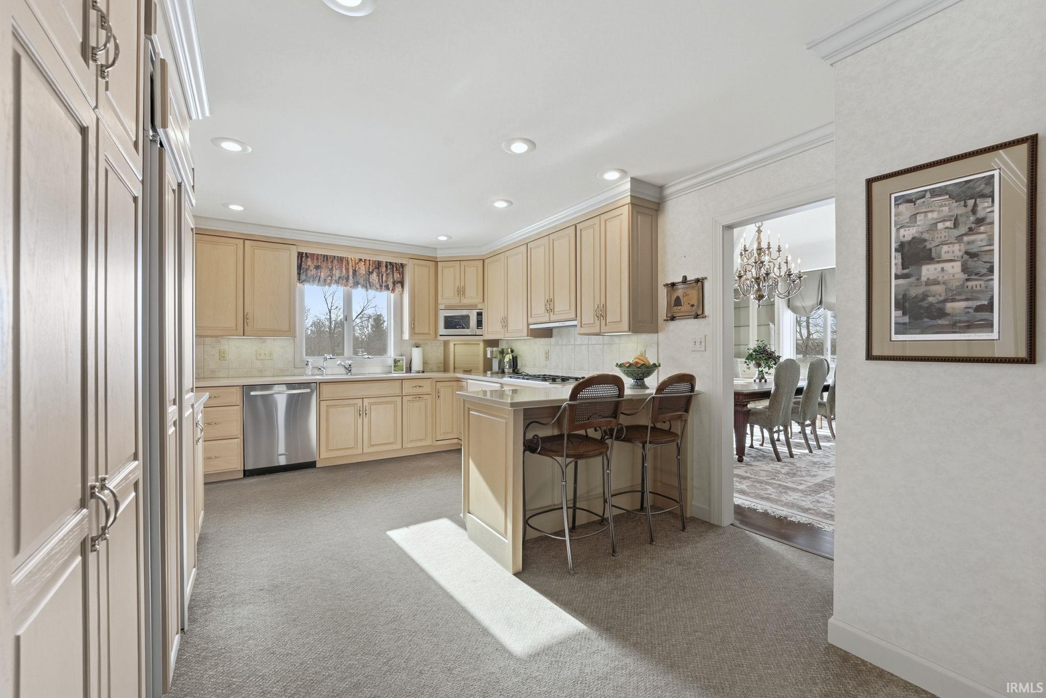 Kitchen featuring light brown cabinets, ornamental molding, a kitchen bar, light colored carpet, and stainless steel appliances