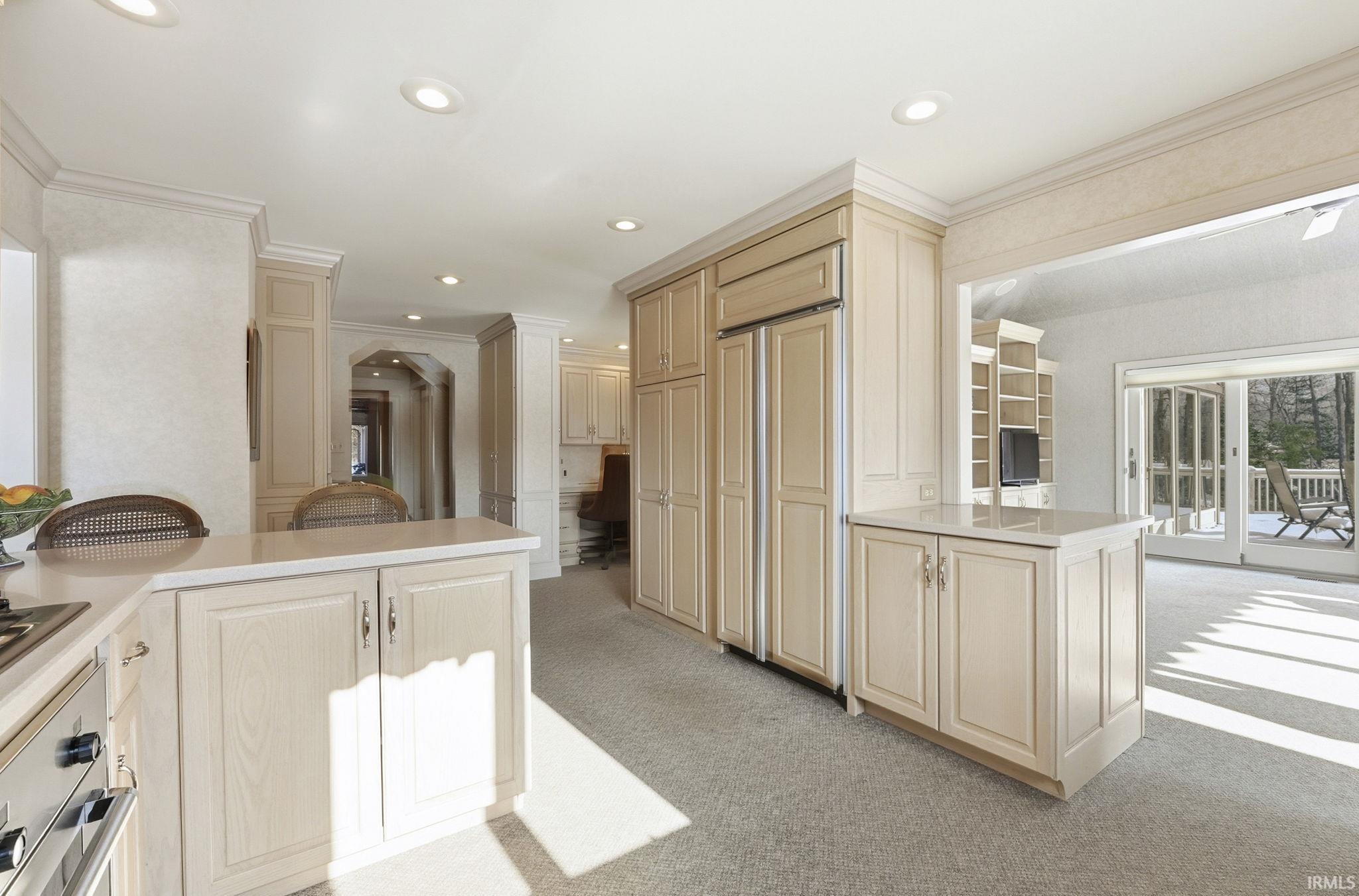 Kitchen featuring a peninsula, light colored carpet, ornamental molding, light countertops, and stainless steel oven