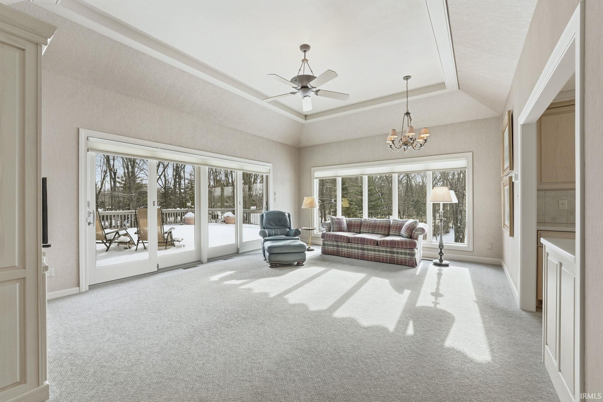 Living room with ceiling fan, light colored carpet, a chandelier, and a tray ceiling