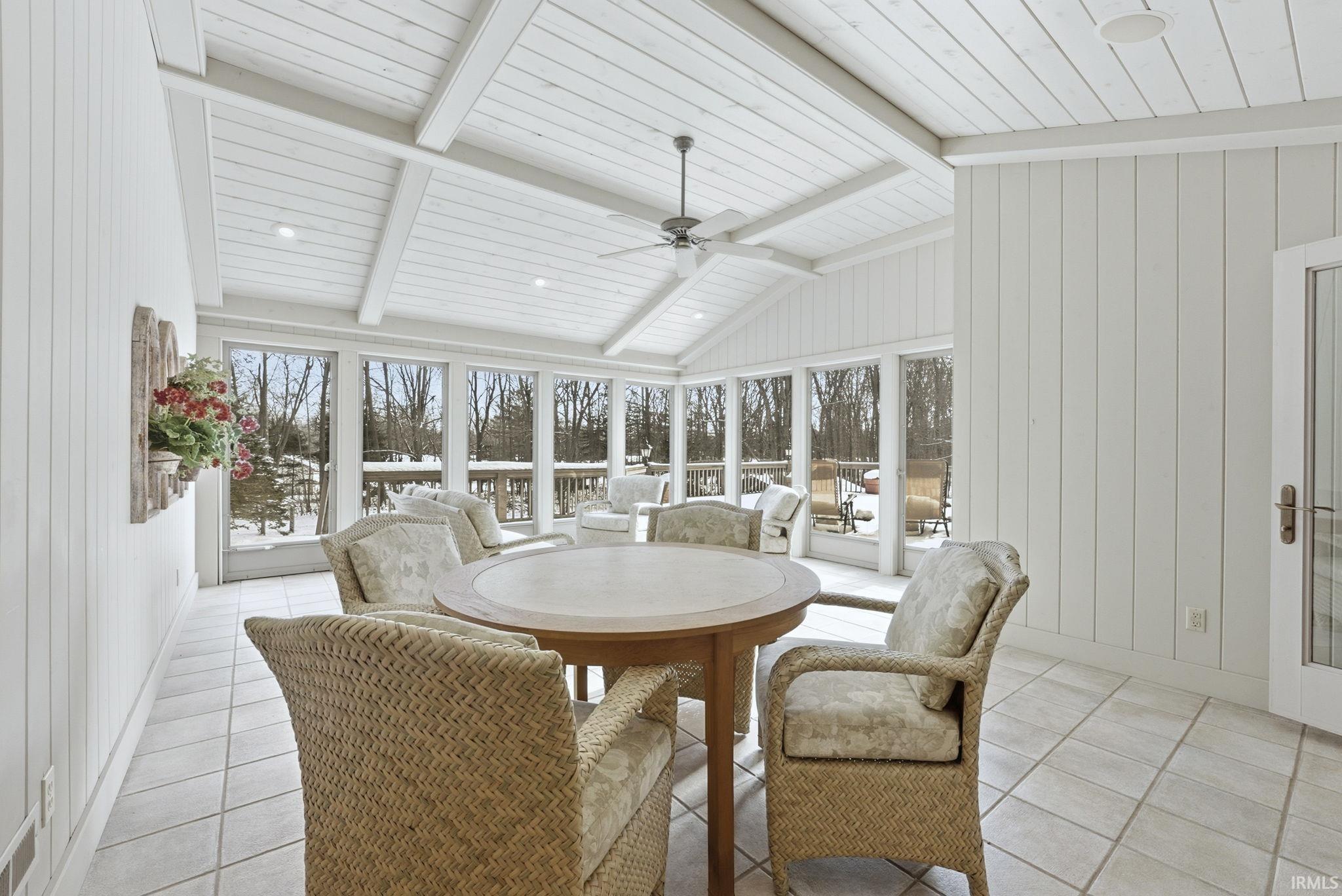 Sunroom / solarium featuring a ceiling fan, tile patterned flooring, wood walls, and outdoor dining space