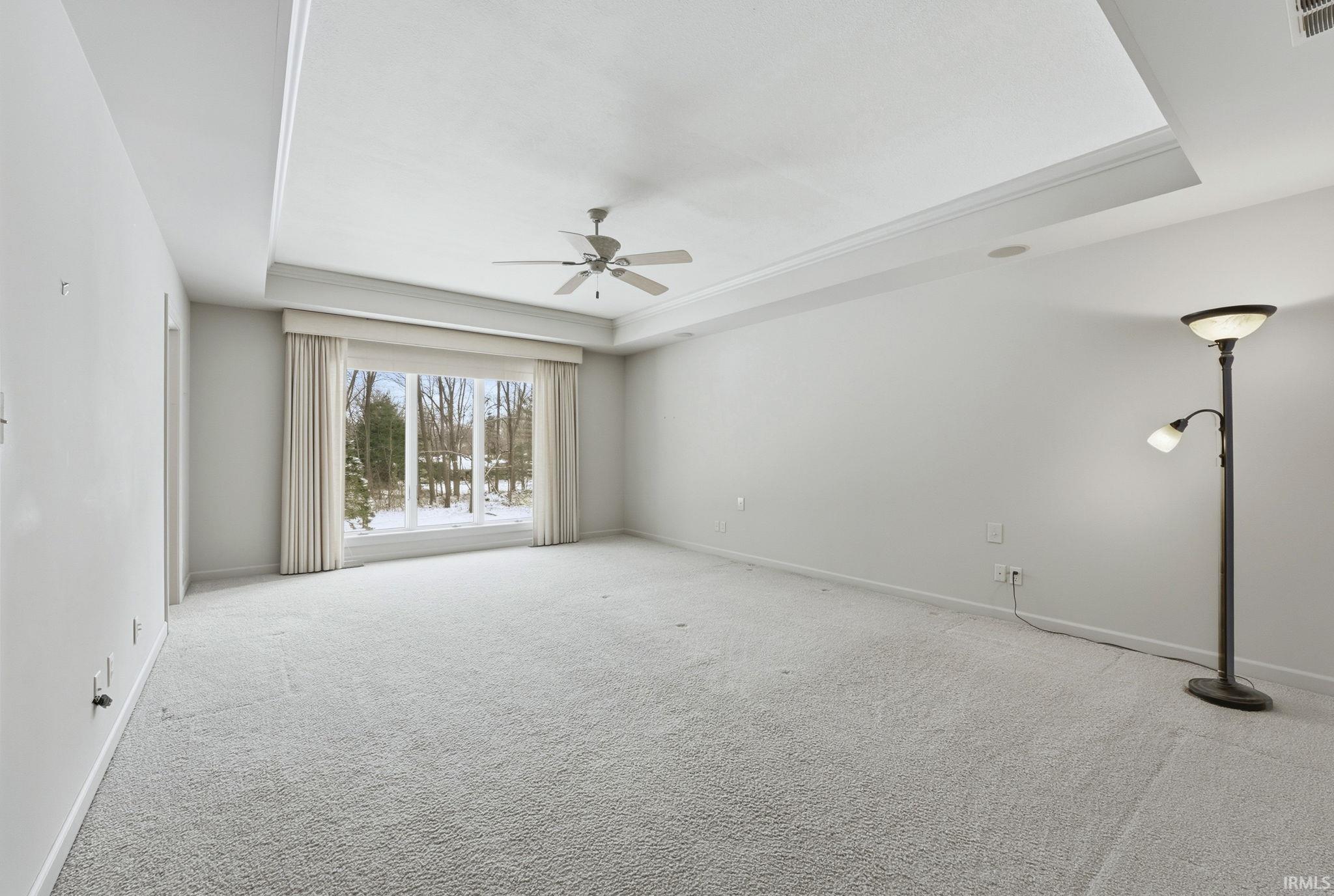 Unfurnished room featuring a tray ceiling, light carpet, and ceiling fan
