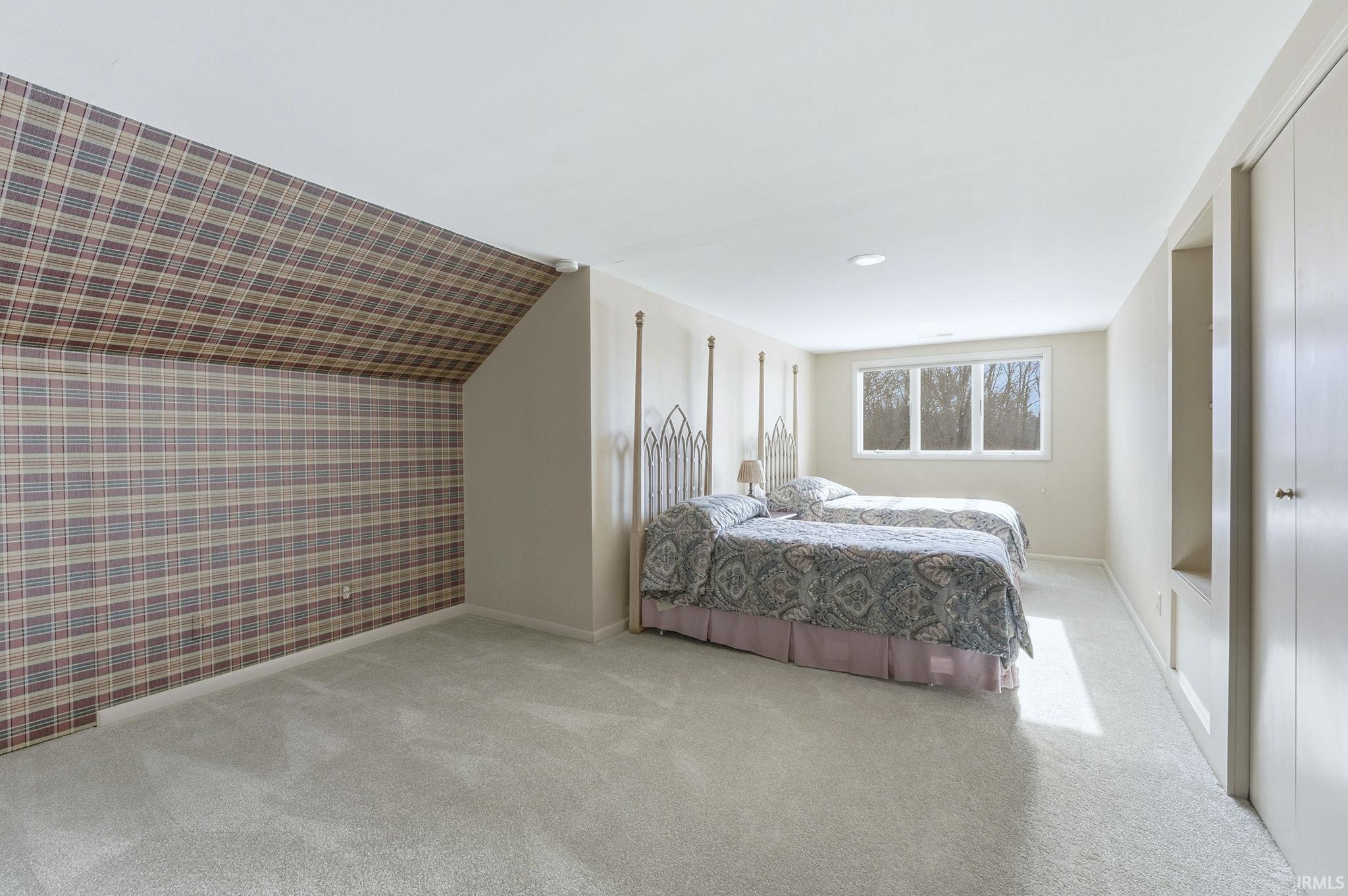 Bedroom featuring wallpapered walls, light carpet, an accent wall, and vaulted ceiling