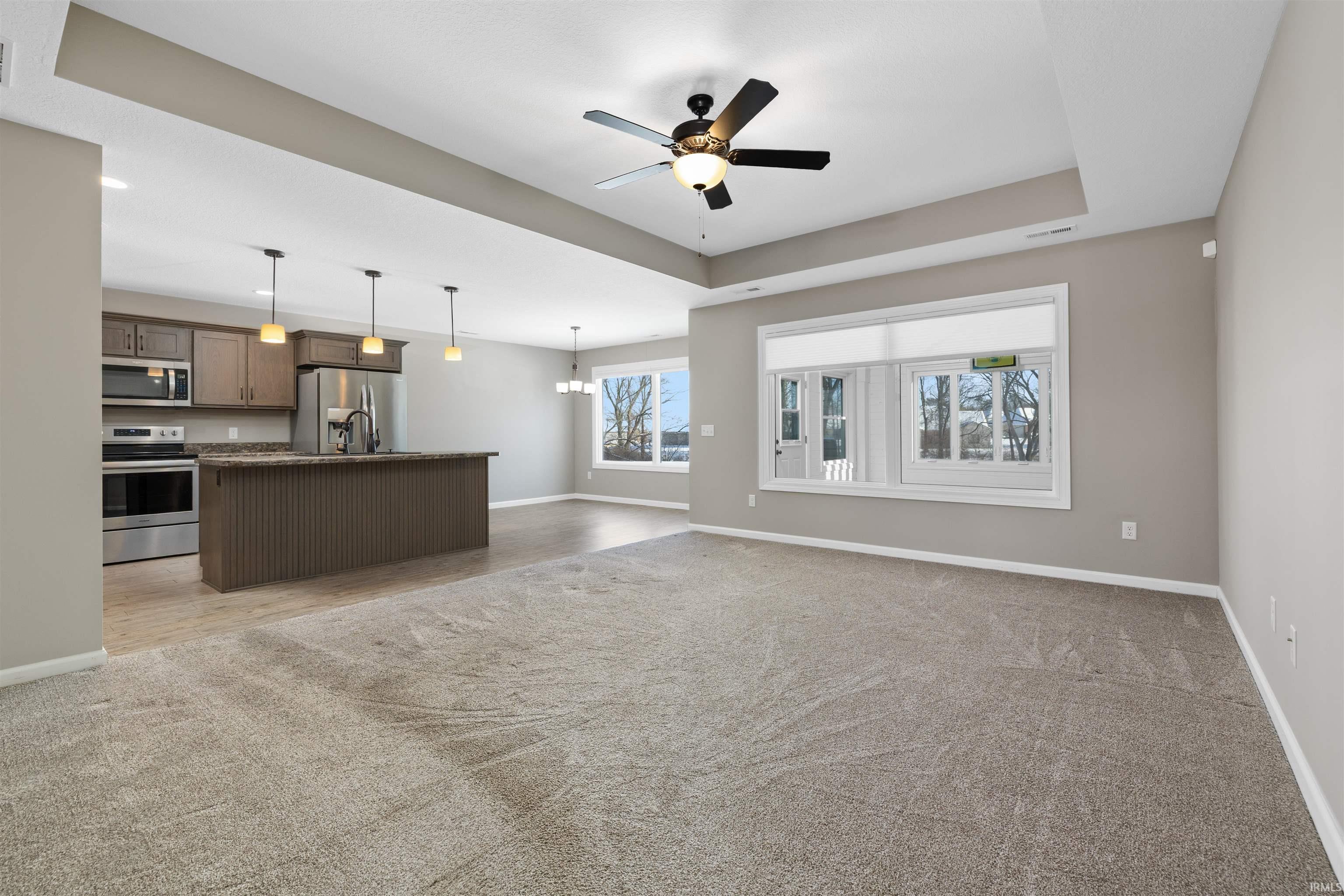 Unfurnished living room with a raised ceiling, ceiling fan, a chandelier, and light carpet