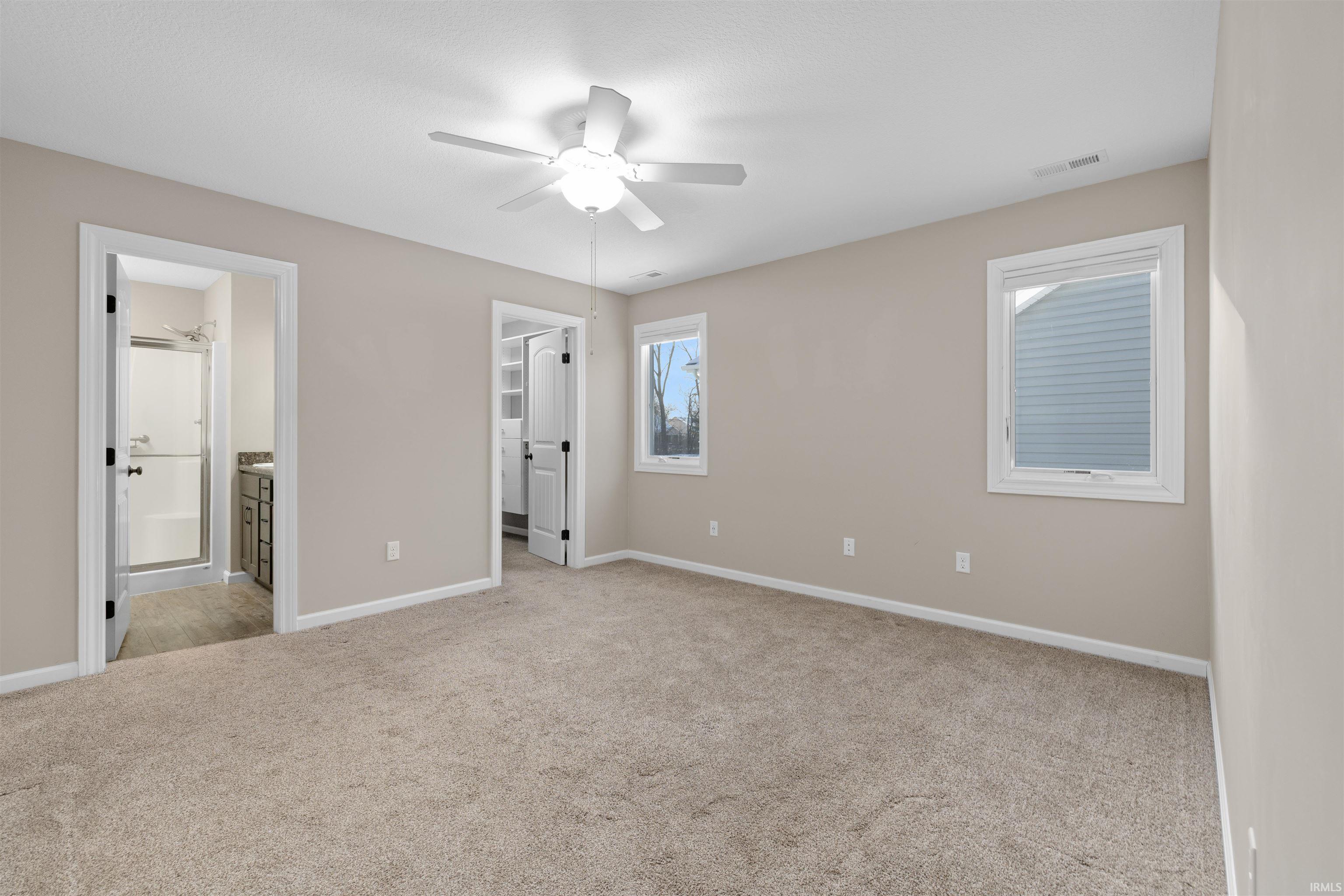 Unfurnished bedroom featuring a walk in closet, light carpet, ensuite bathroom, and a ceiling fan