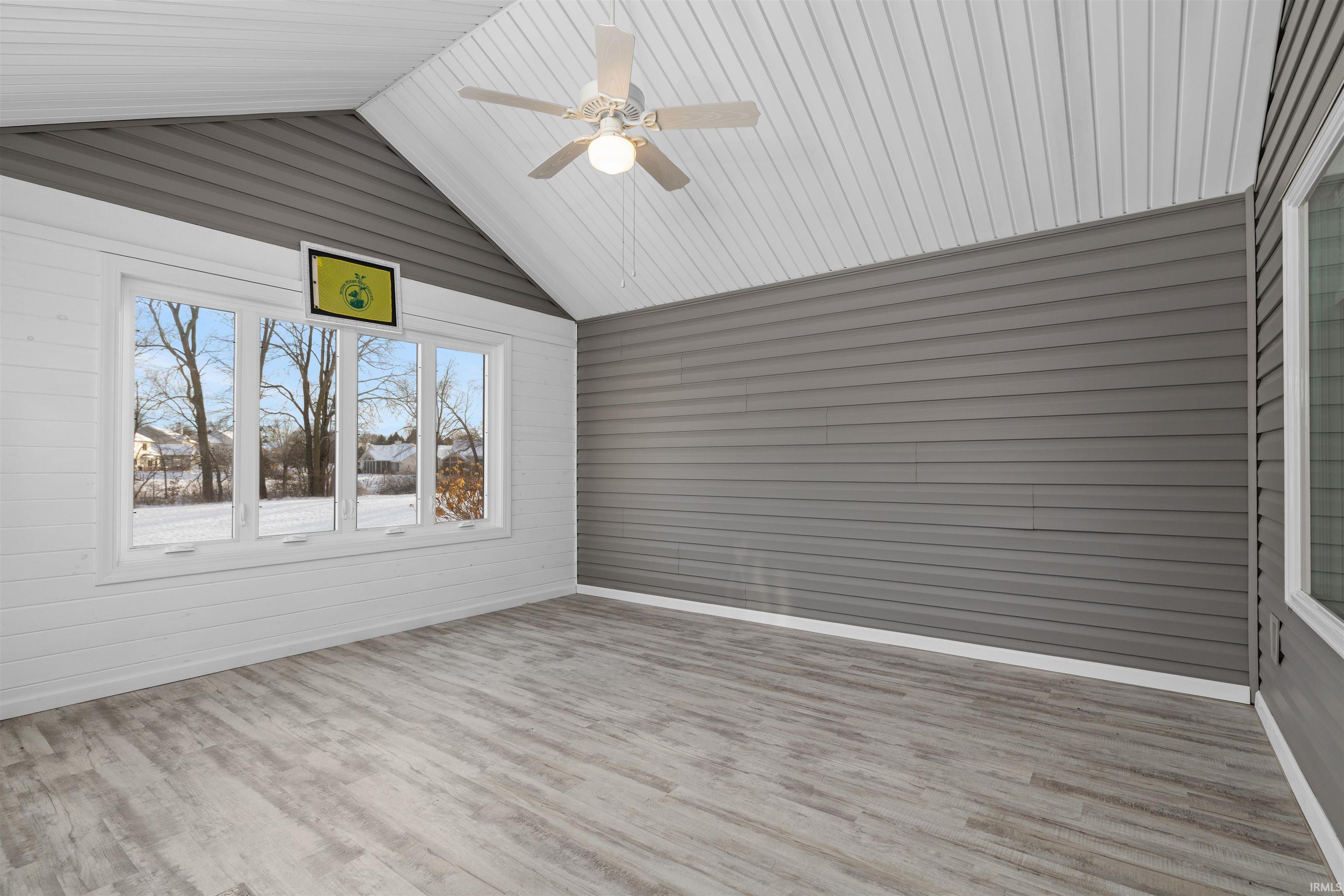 Empty room with wood walls, wood finished floors, vaulted ceiling, and a ceiling fan