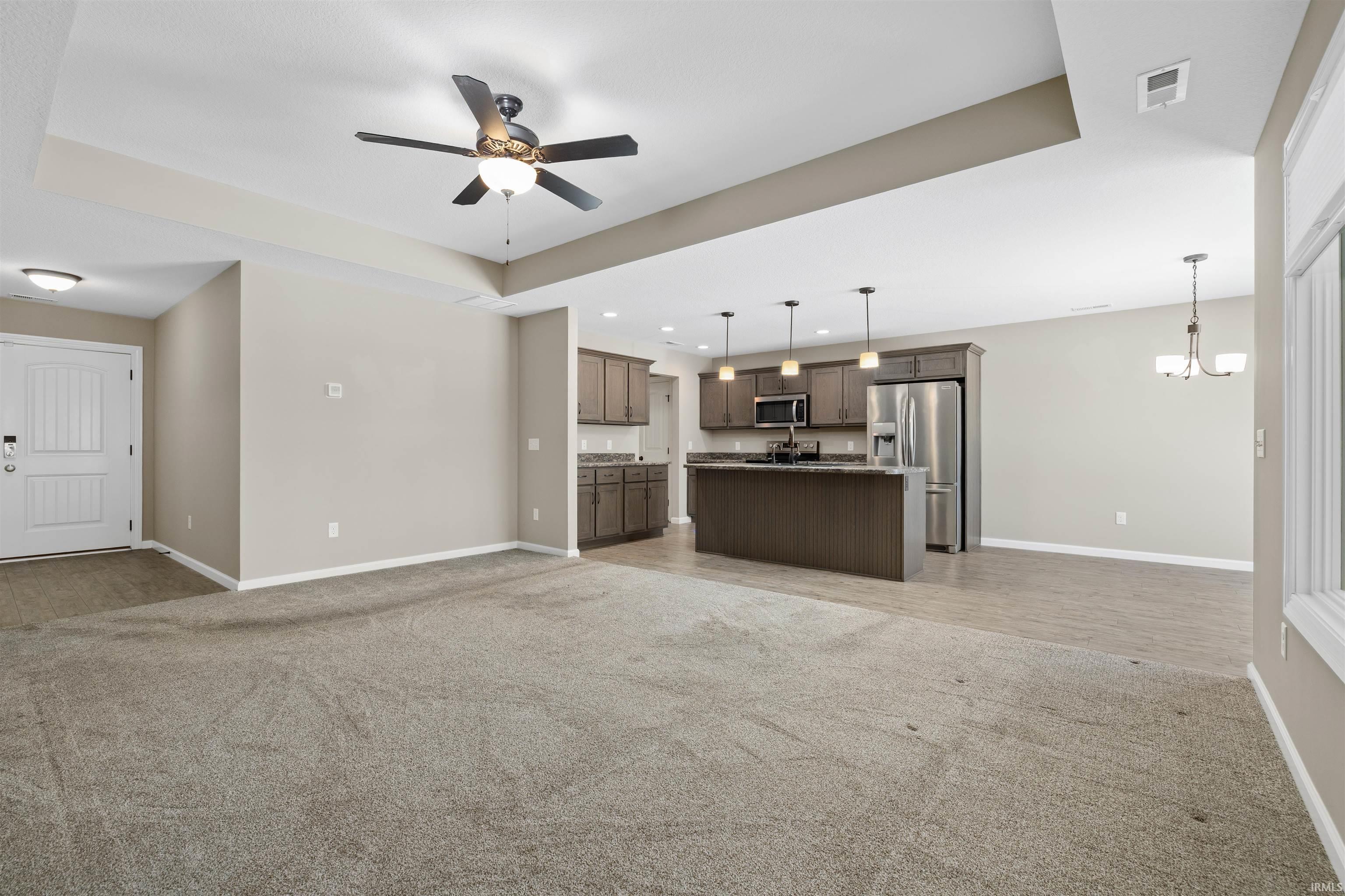 Unfurnished living room with a raised ceiling, light carpet, a chandelier, and recessed lighting