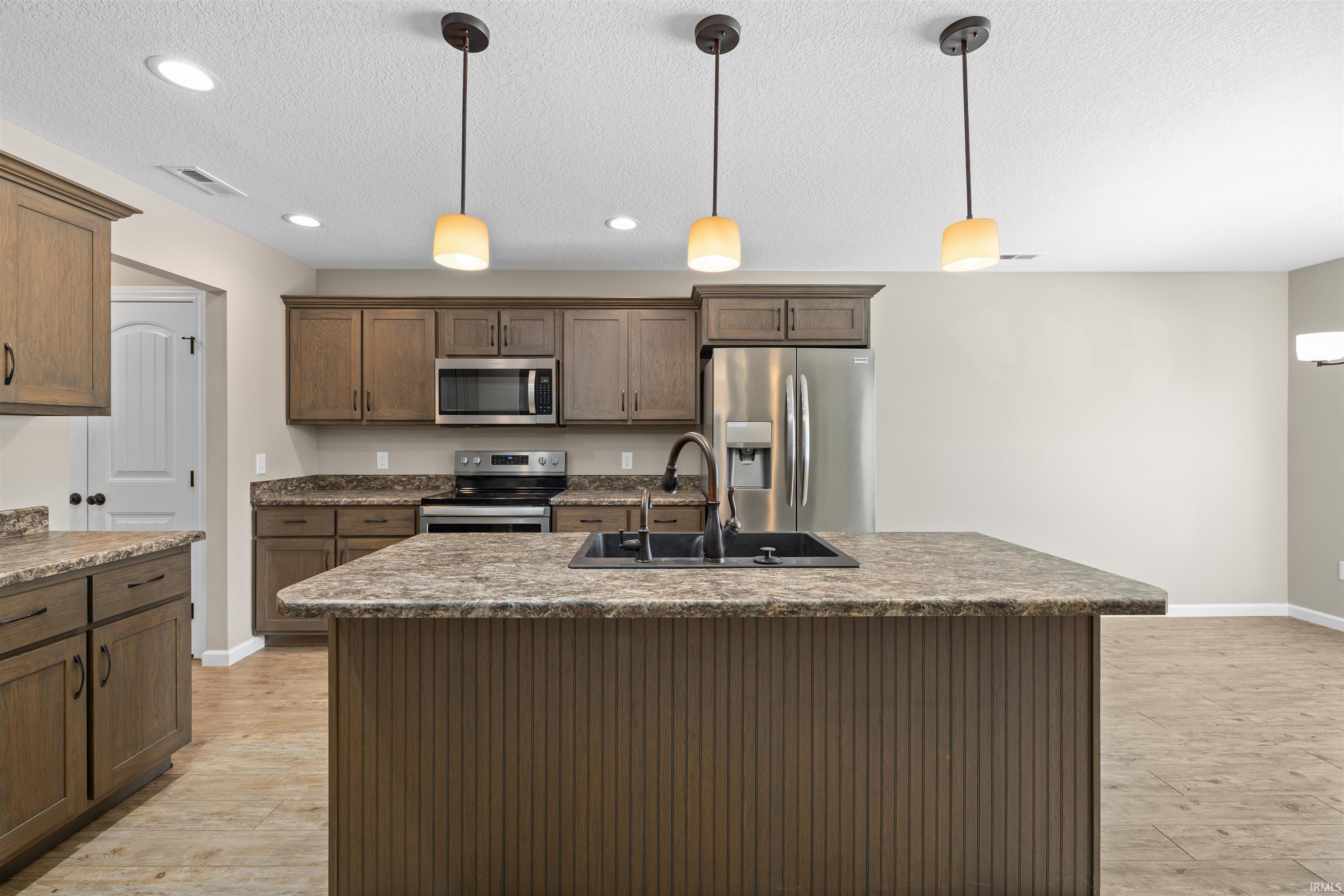 Kitchen with hanging light fixtures, appliances with stainless steel finishes, a center island with sink, a textured ceiling, and recessed lighting