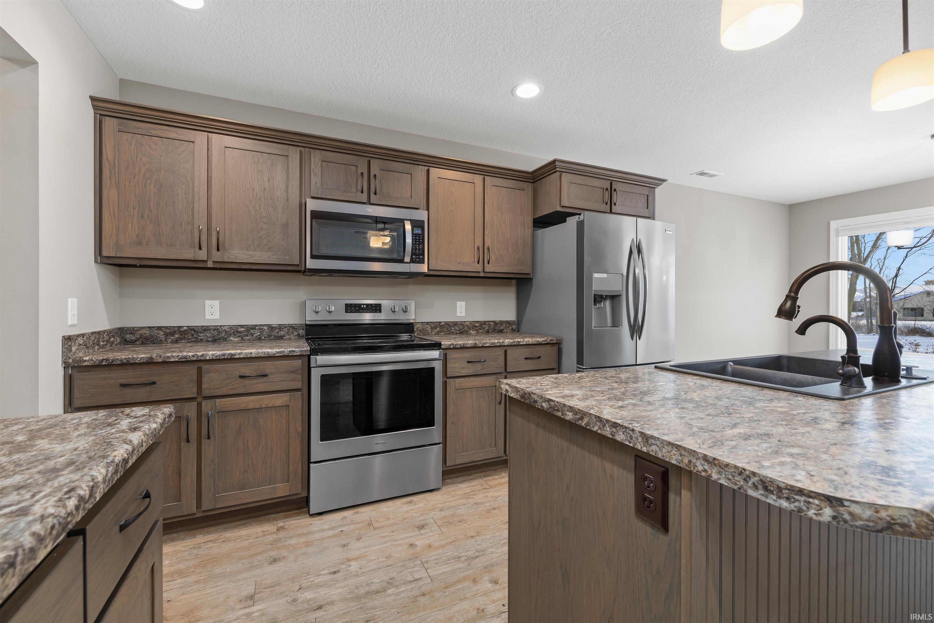 Kitchen with appliances with stainless steel finishes, recessed lighting, light wood-style floors, pendant lighting, and a textured ceiling