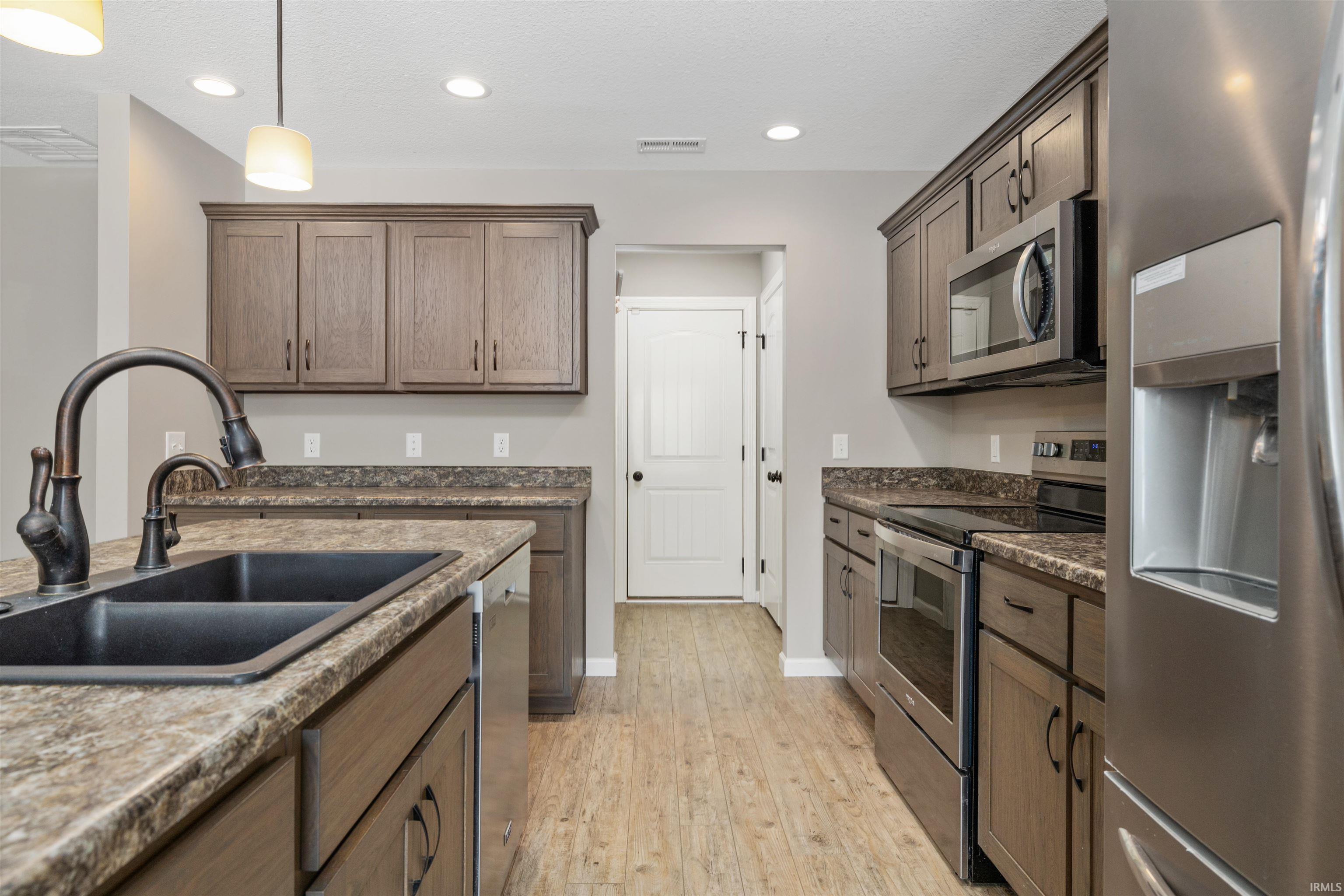 Kitchen with appliances with stainless steel finishes, decorative light fixtures, light wood-style flooring, recessed lighting, and dark stone counters