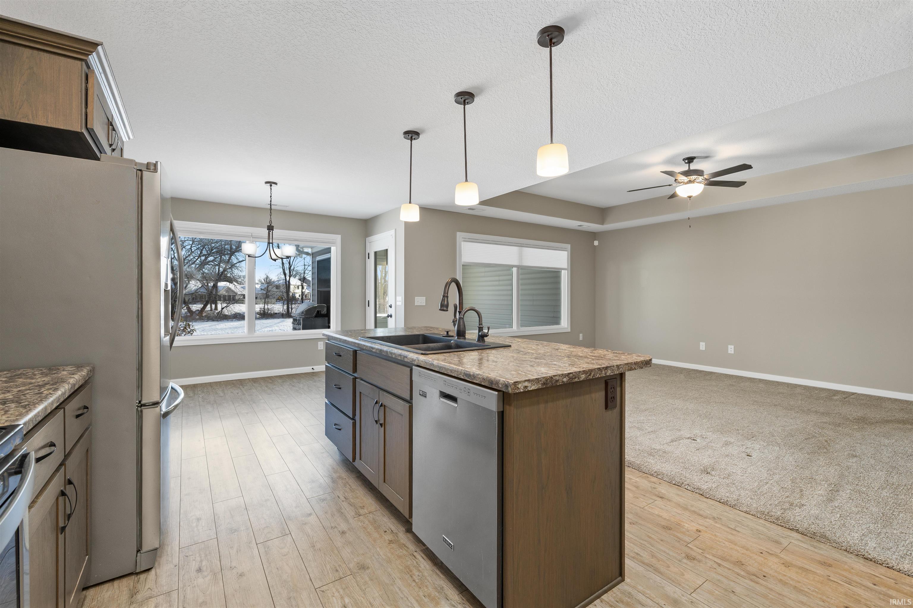 Kitchen featuring pendant lighting, open floor plan, stainless steel appliances, a center island with sink, and light wood finished floors