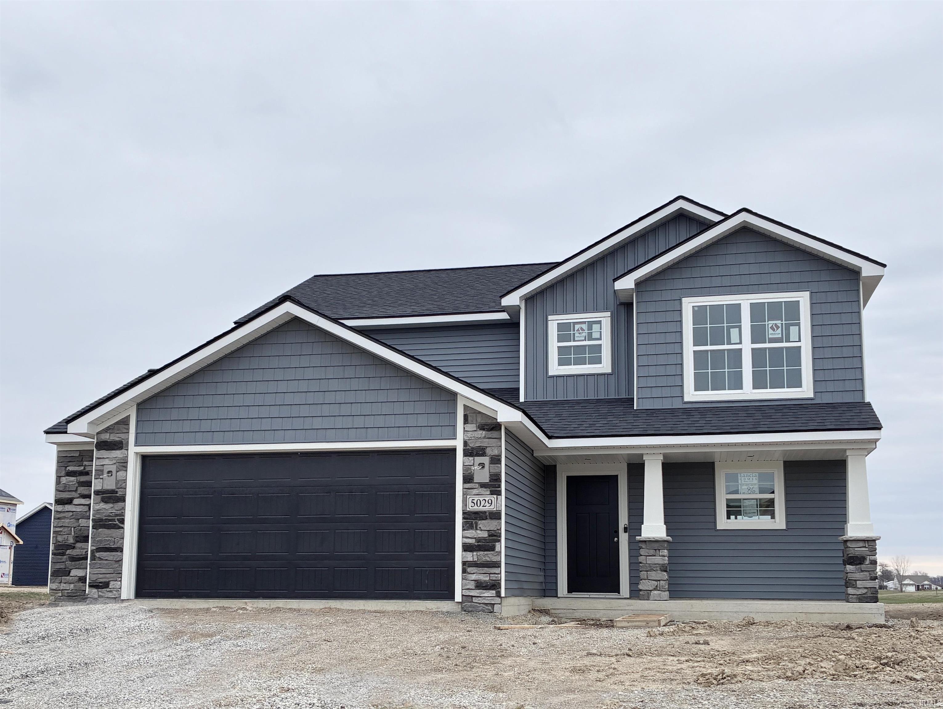 Craftsman-style home featuring an attached garage, covered porch, roof with shingles, and dirt driveway