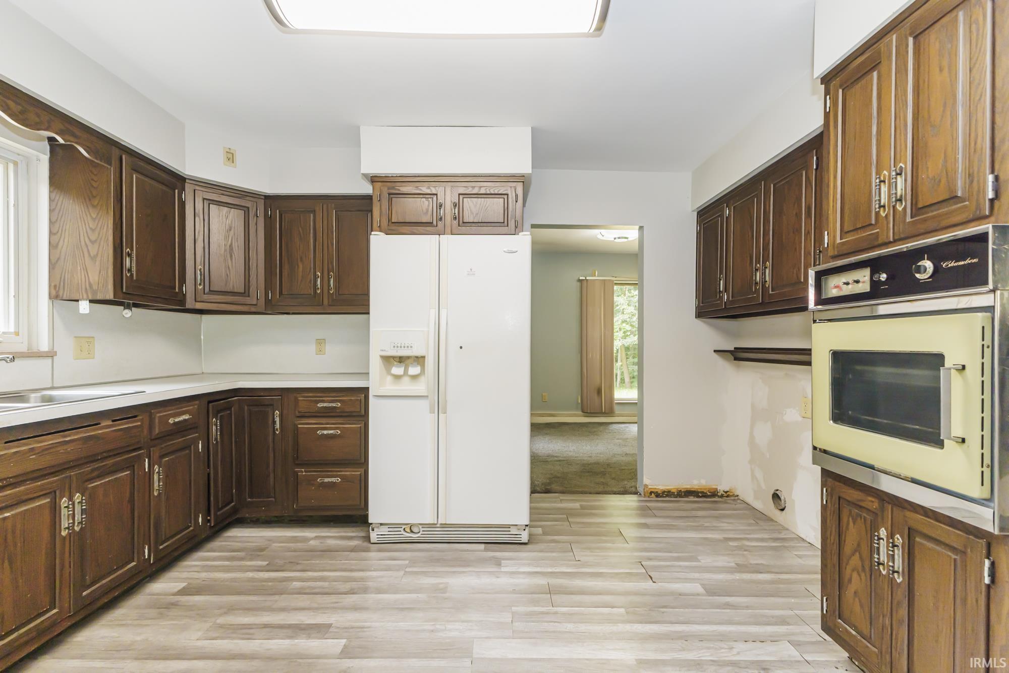 Kitchen with extensive wood cabinetry, wood-finish flooring, a built-in oven, and a double-basin sink