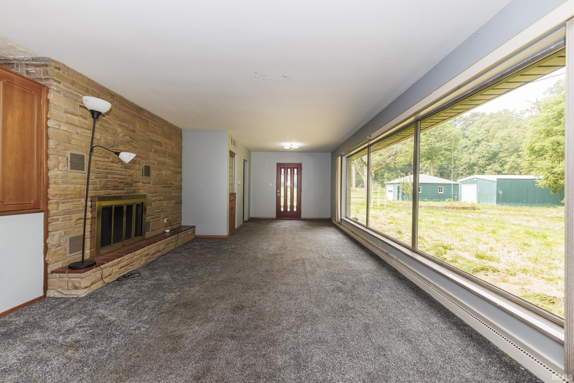 Living area featuring a floor-to-ceiling window, a wood-burning fireplace with a stone surround, and carpet flooring