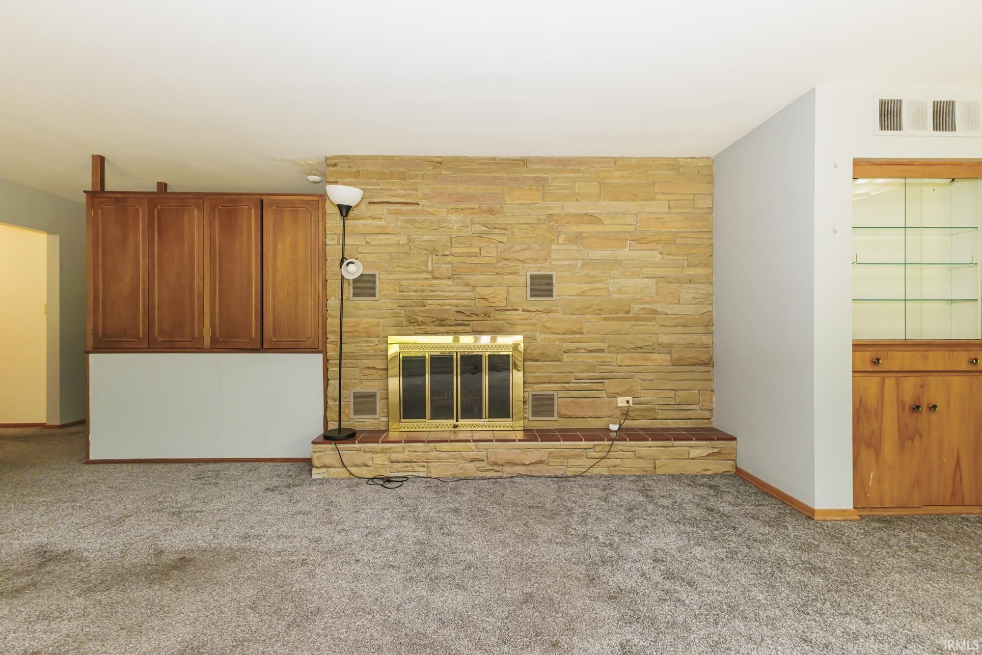 Stone fireplace with a brass firebox, flanked by built-in wood cabinetry and a display cabinet with glass shelving