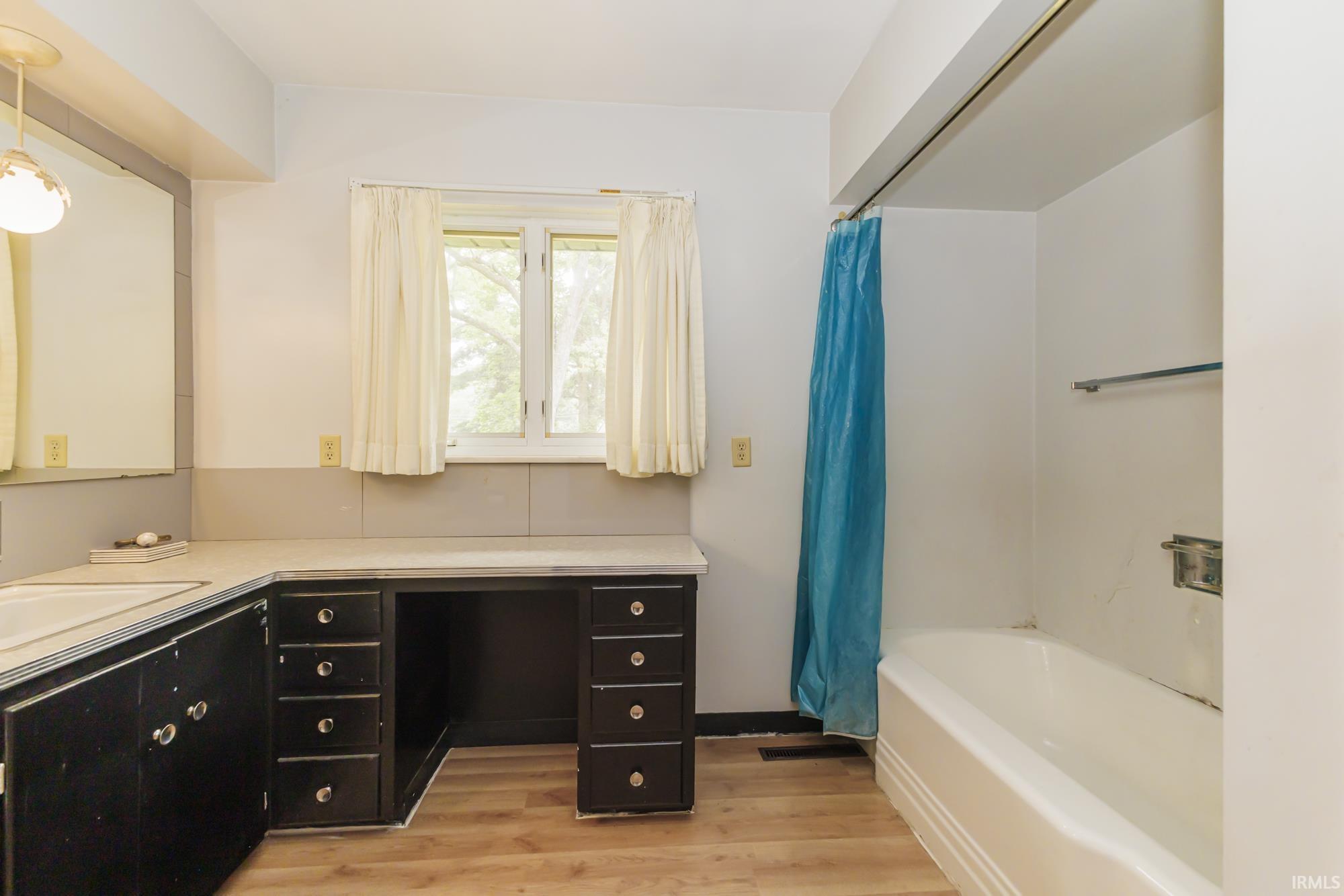Bathroom featuring a white bathtub, wood-finish flooring, a window, and a built-in vanity with dark cabinetry and an integrated sink