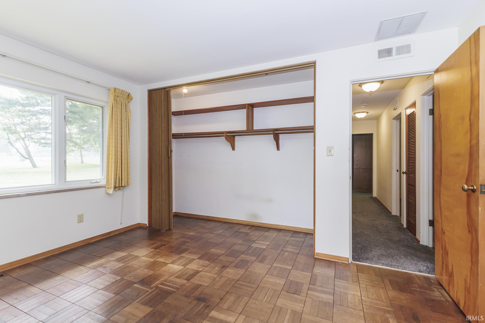 Room featuring wood-finish parquet flooring, a wide window, and a built-in closet with shelving and hanging rods