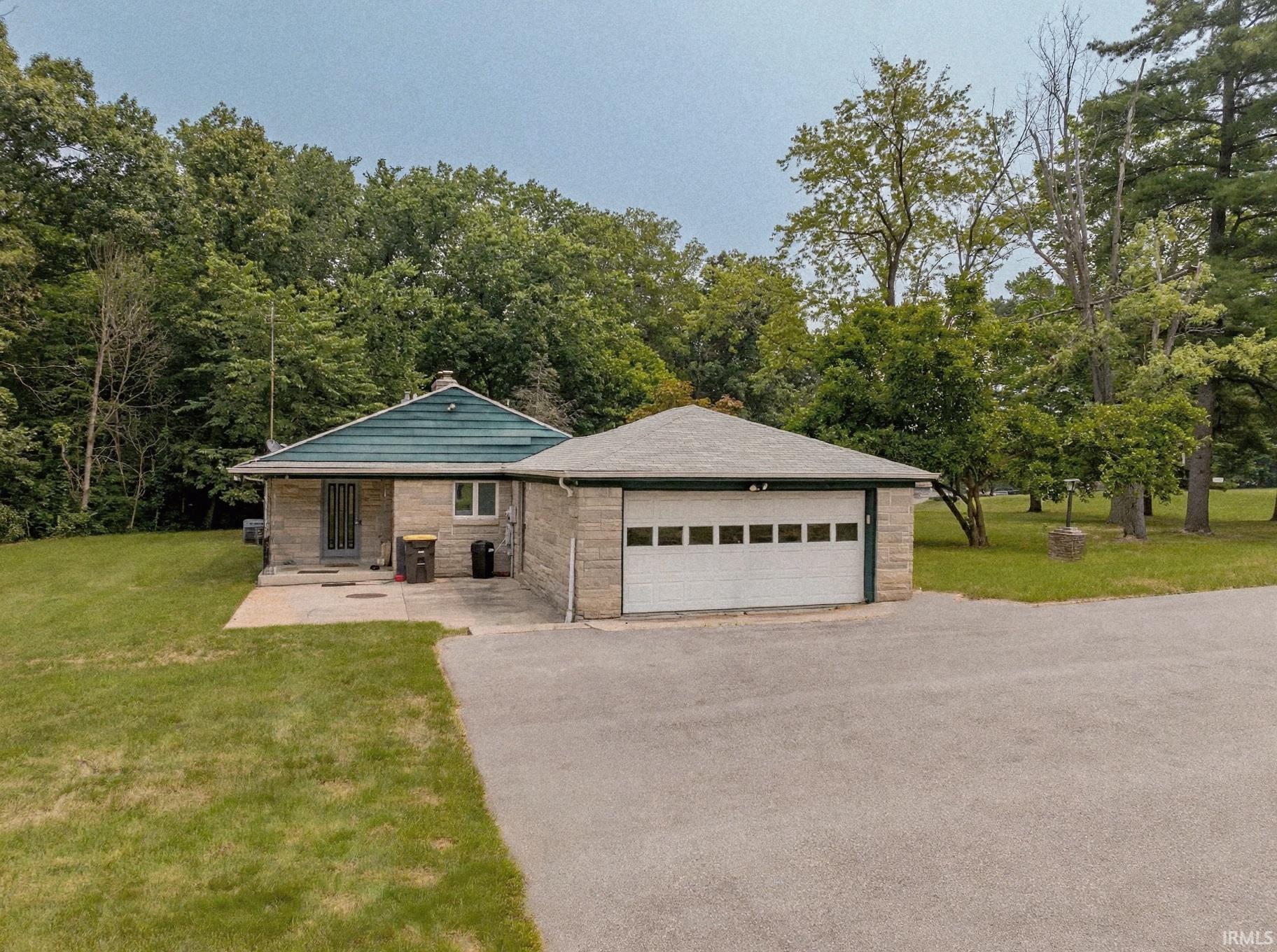 Stone exterior home with an attached two-car garage, featuring a concrete driveway and mature trees surrounding the property