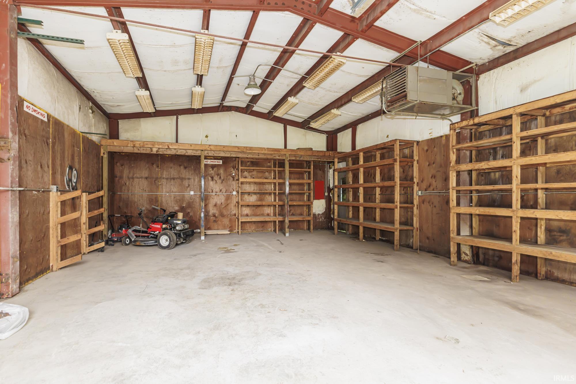 Spacious interior featuring a concrete floor, exposed structural beams, ceiling-mounted fluorescent lighting, and built-in wood shelving units