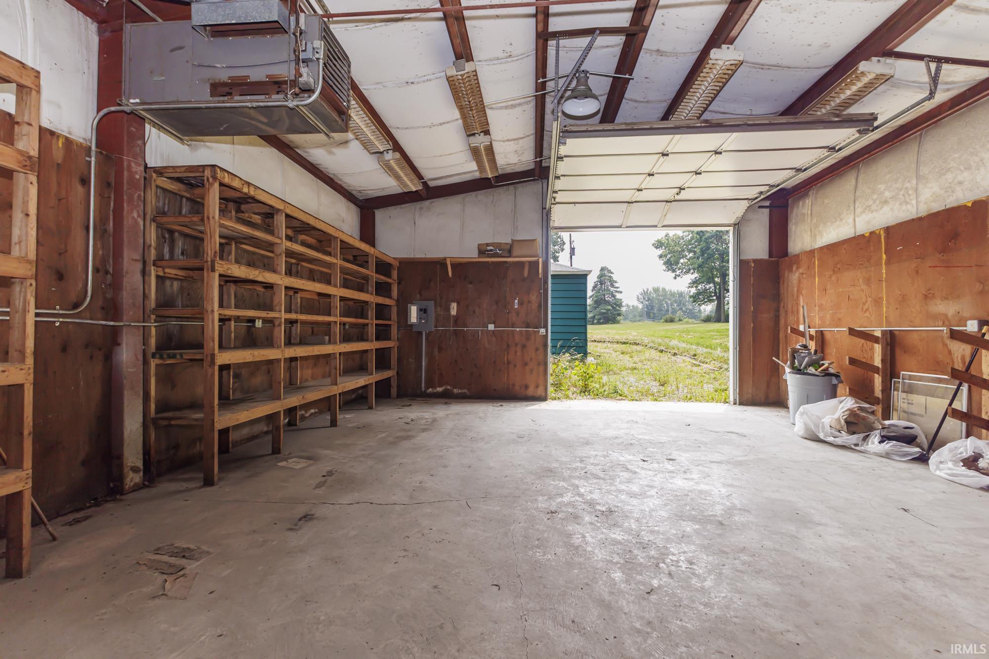 Spacious interior featuring a concrete floor, plywood walls, metal ceiling with exposed beams, and a large overhead door