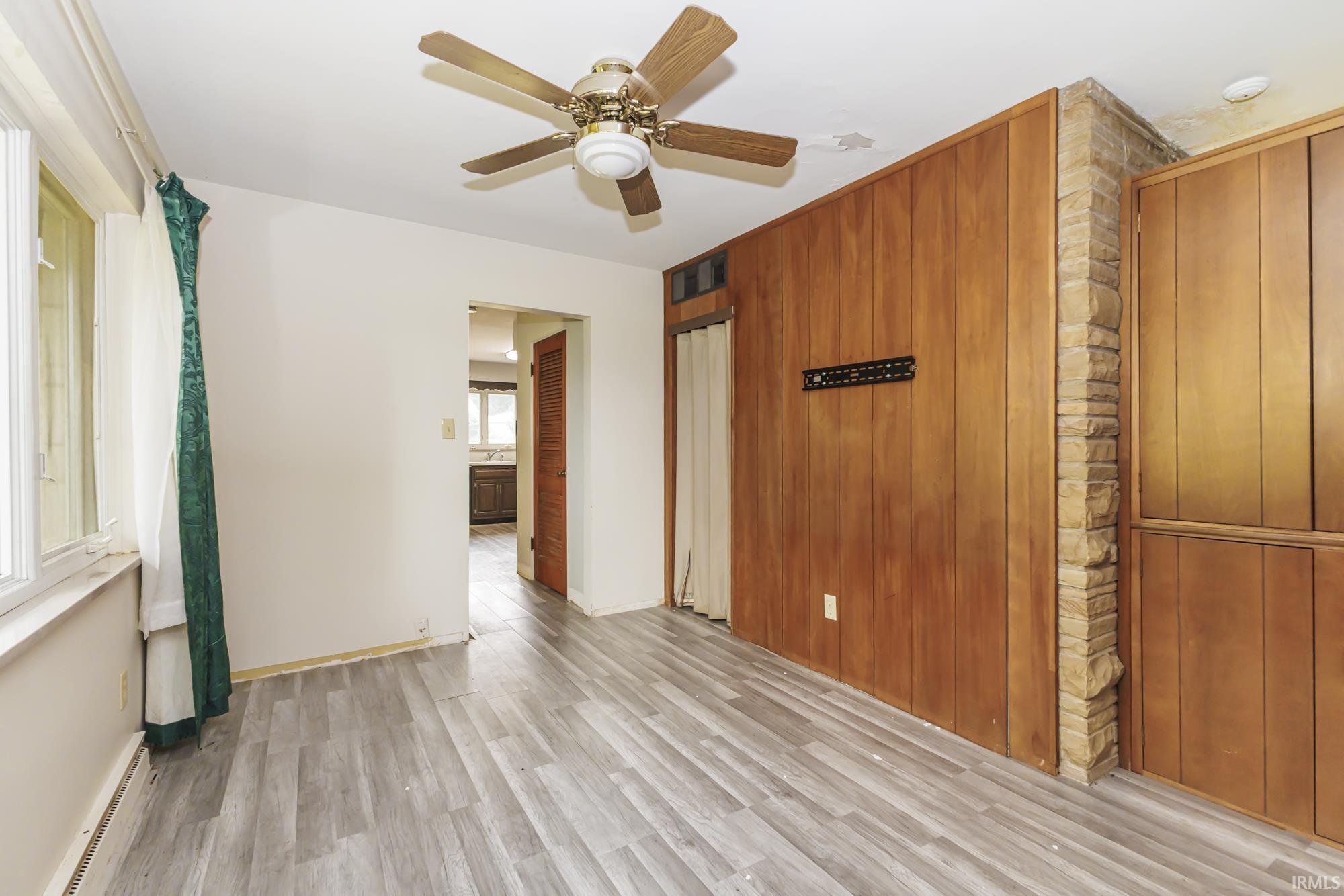 Room featuring wood-finish flooring, a ceiling fan, paneled accent wall, and a stone column detail
