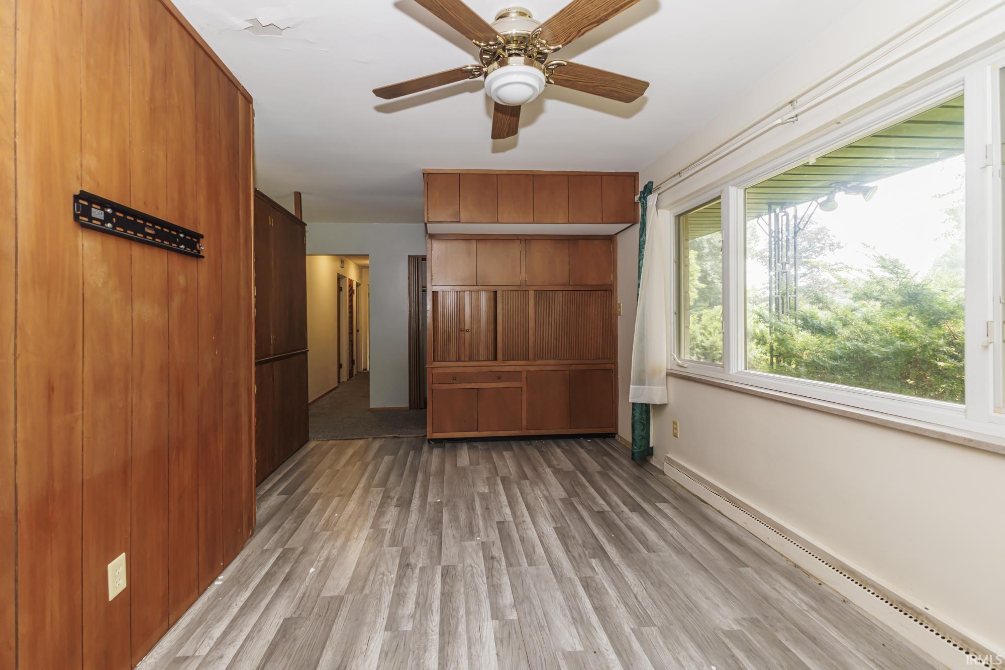 Interior space featuring wood-finish flooring, a wall-mounted wood-panel feature, and a large window with exterior foliage visible