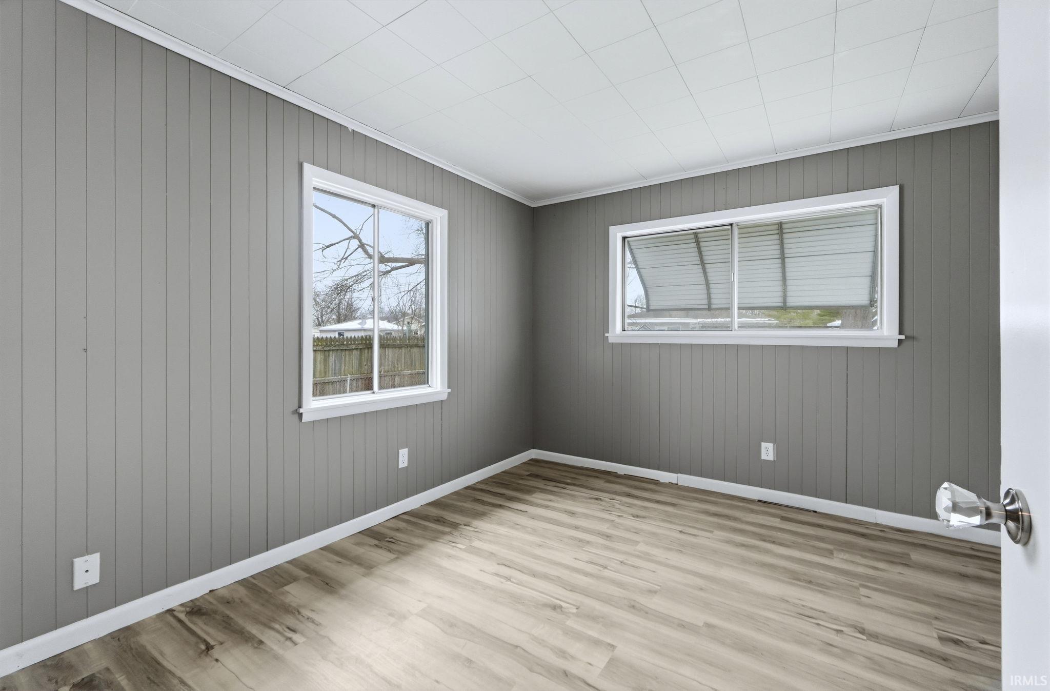 Empty room featuring light wood-style floors, wood walls, and crown molding