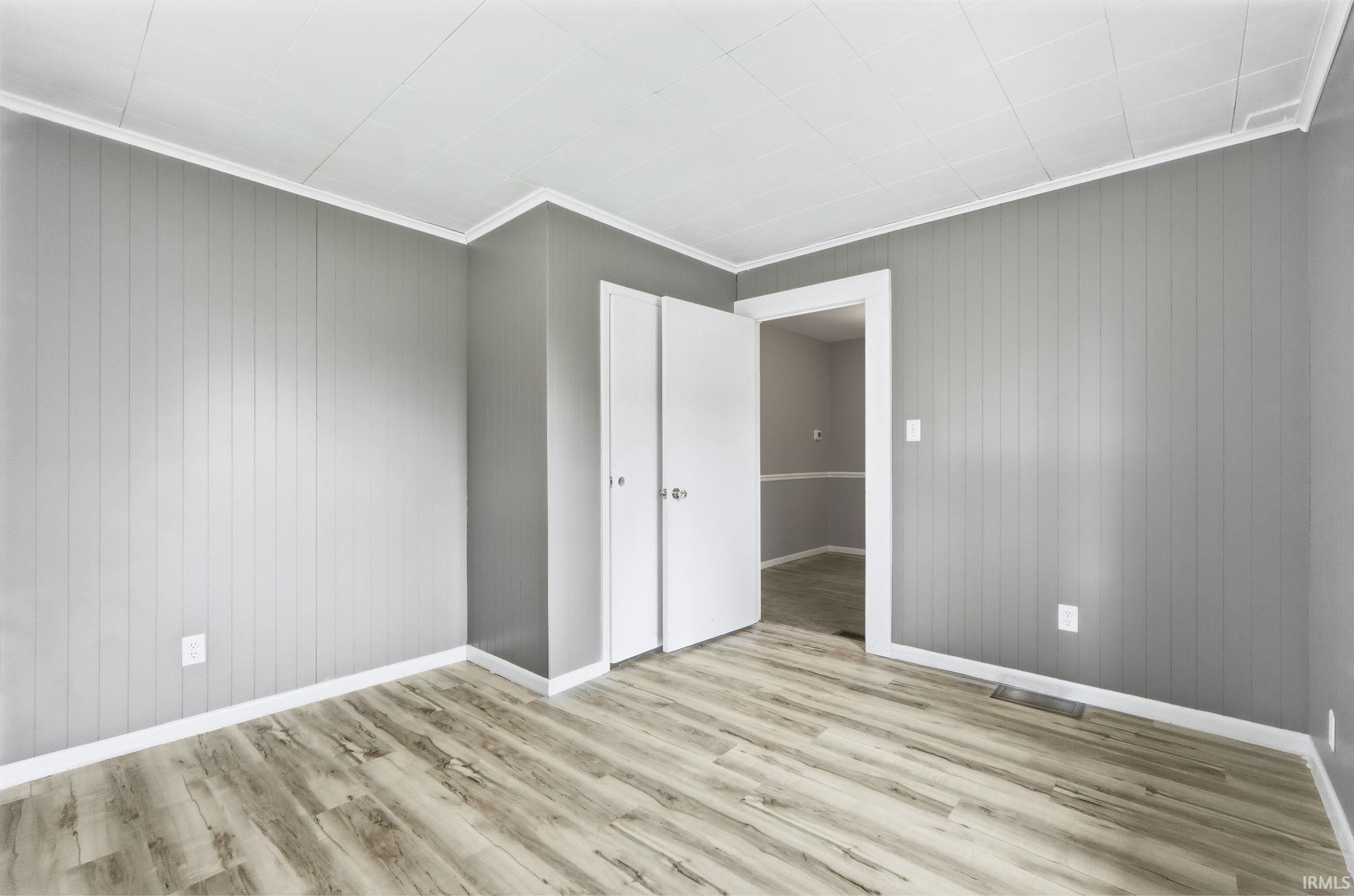 Unfurnished bedroom with wooden walls, wood finished floors, and ornamental molding