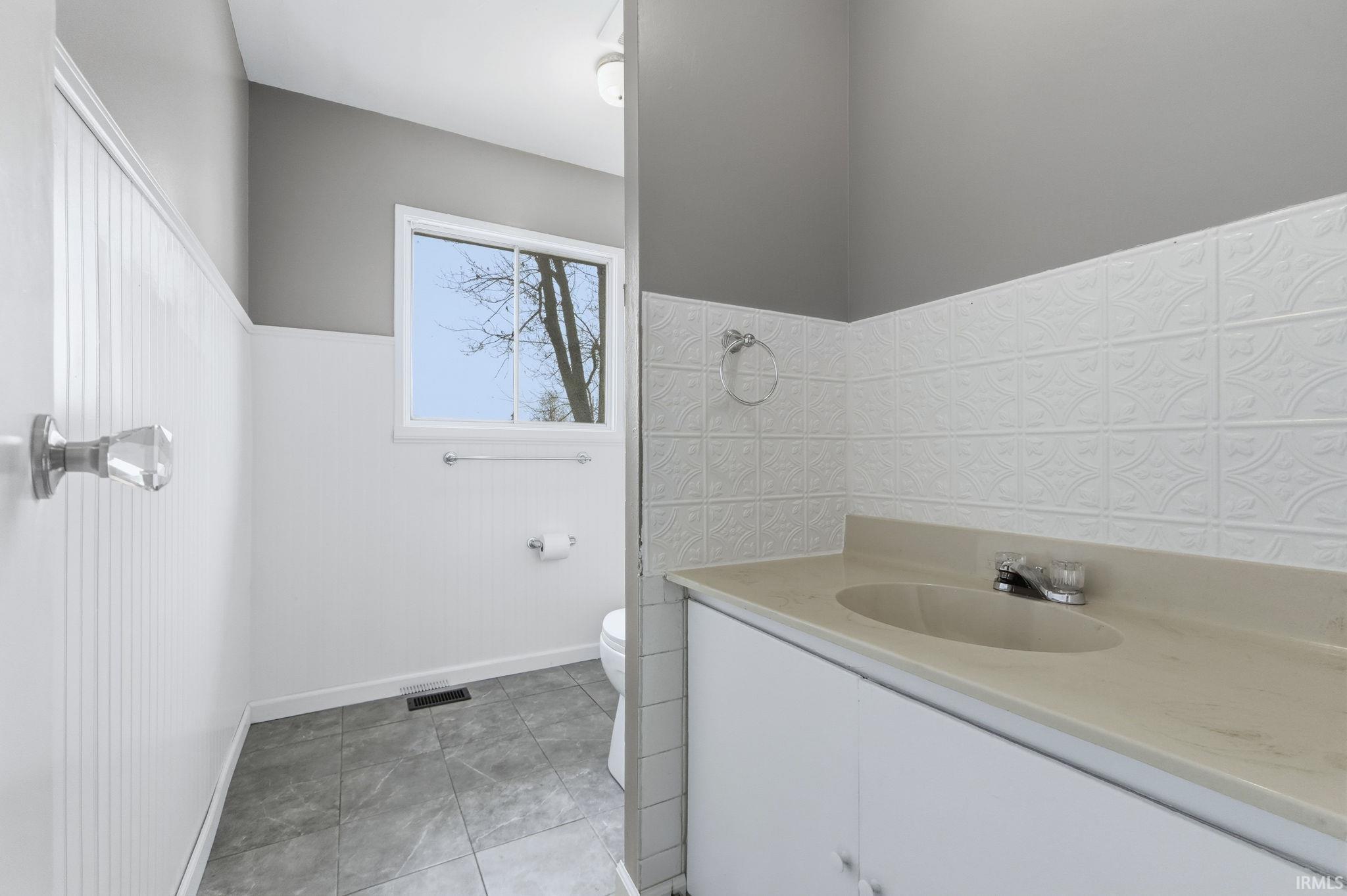 Full bath with vanity, light tile patterned flooring, and a wainscoted wall