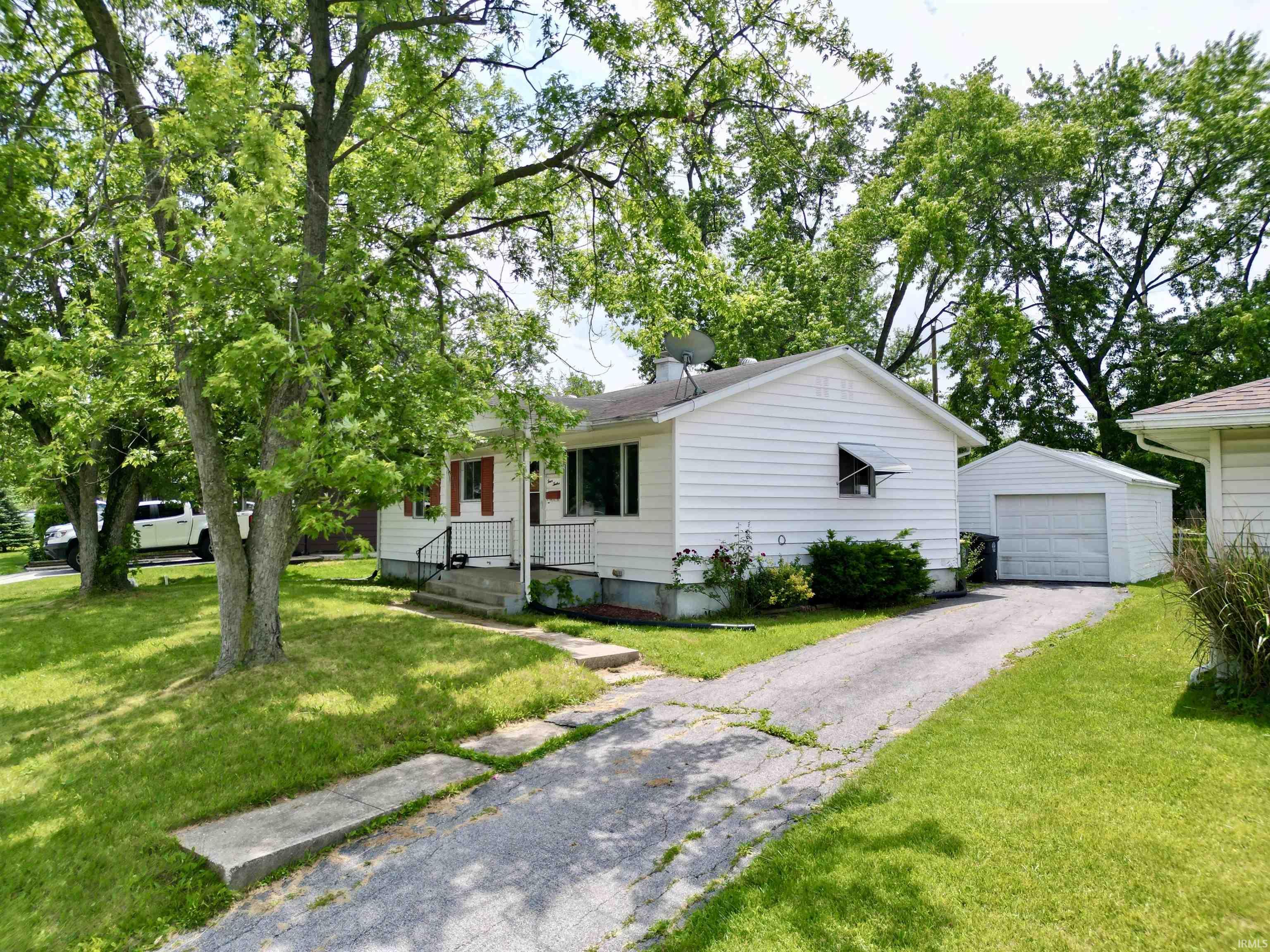 White siding residence with a covered front porch and a paved driveway leading to a detached single-car garage