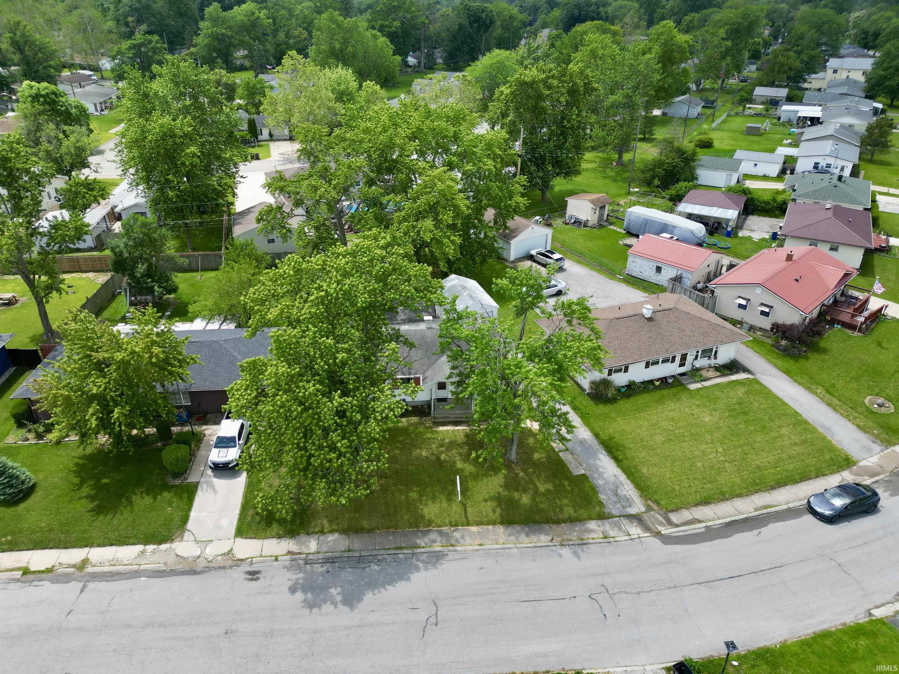 Suburban residential street featuring multiple single-story homes, mature trees, and manicured lawns