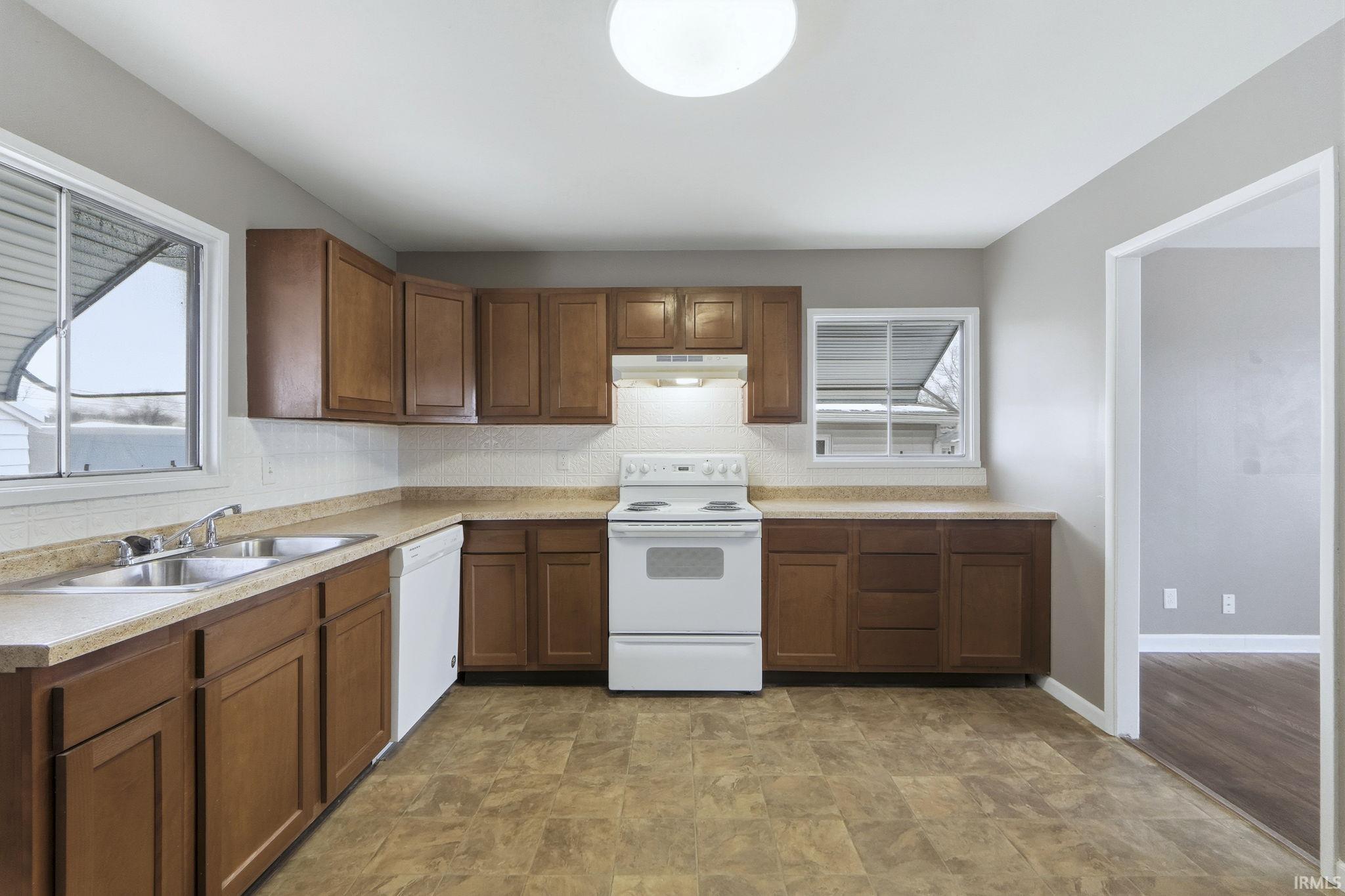 Kitchen featuring white appliances, light countertops, tasteful backsplash, under cabinet range hood, and brown cabinetry