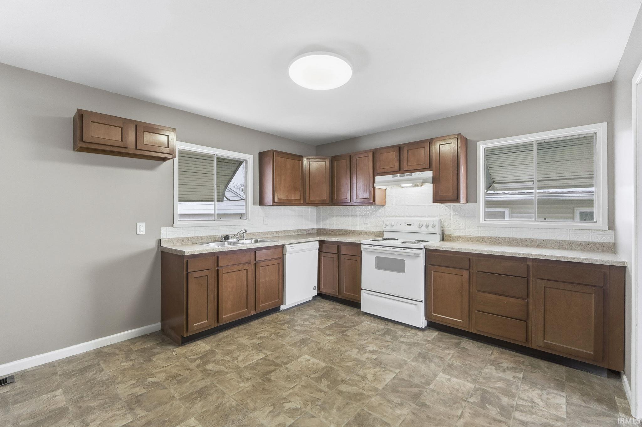 Kitchen with white appliances, light countertops, under cabinet range hood, and stone finish flooring