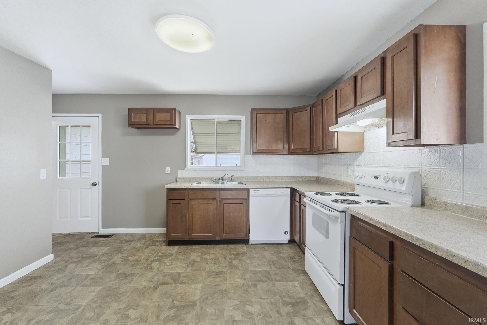 Kitchen featuring white appliances, light countertops, under cabinet range hood, tasteful backsplash, and brown cabinets