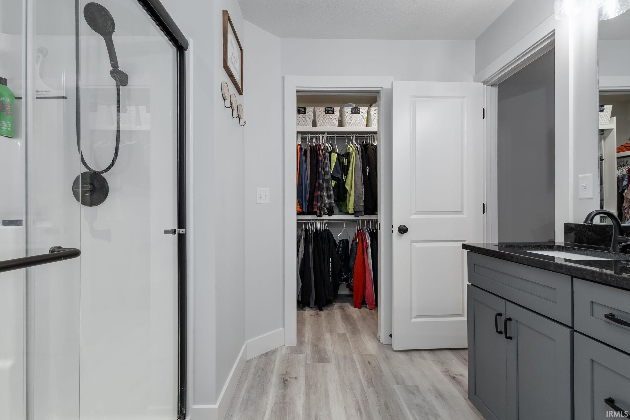 Full bath with a spacious closet, vanity, light wood-type flooring, and a shower stall