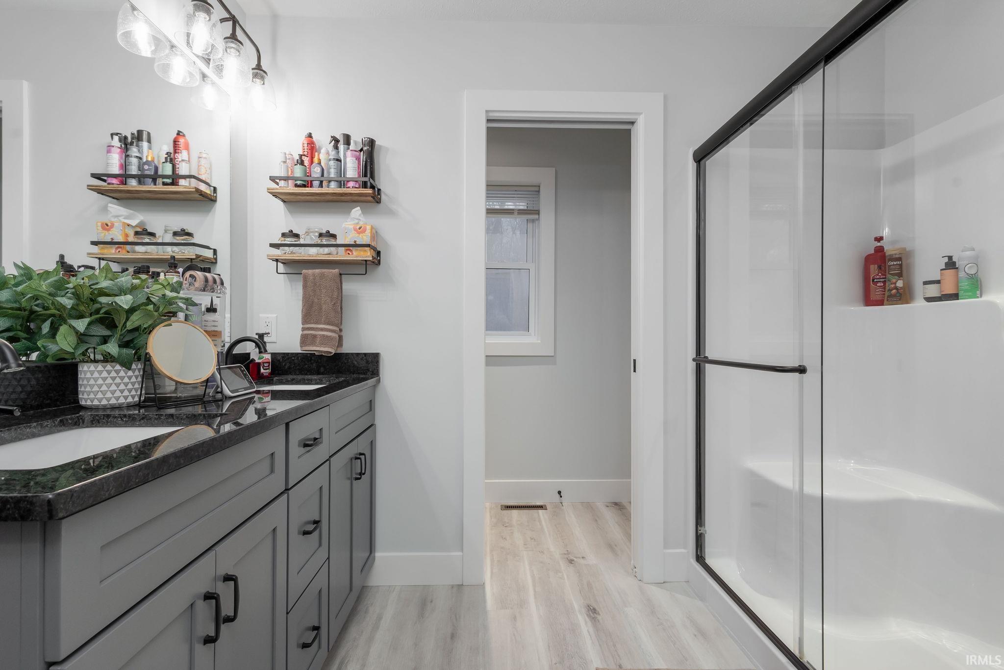 Full bath with double vanity, a stall shower, and light wood-type flooring