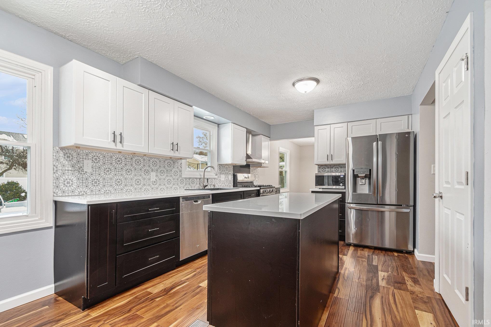Kitchen with white cabinets, stainless steel appliances, a kitchen island, tasteful backsplash, and a textured ceiling