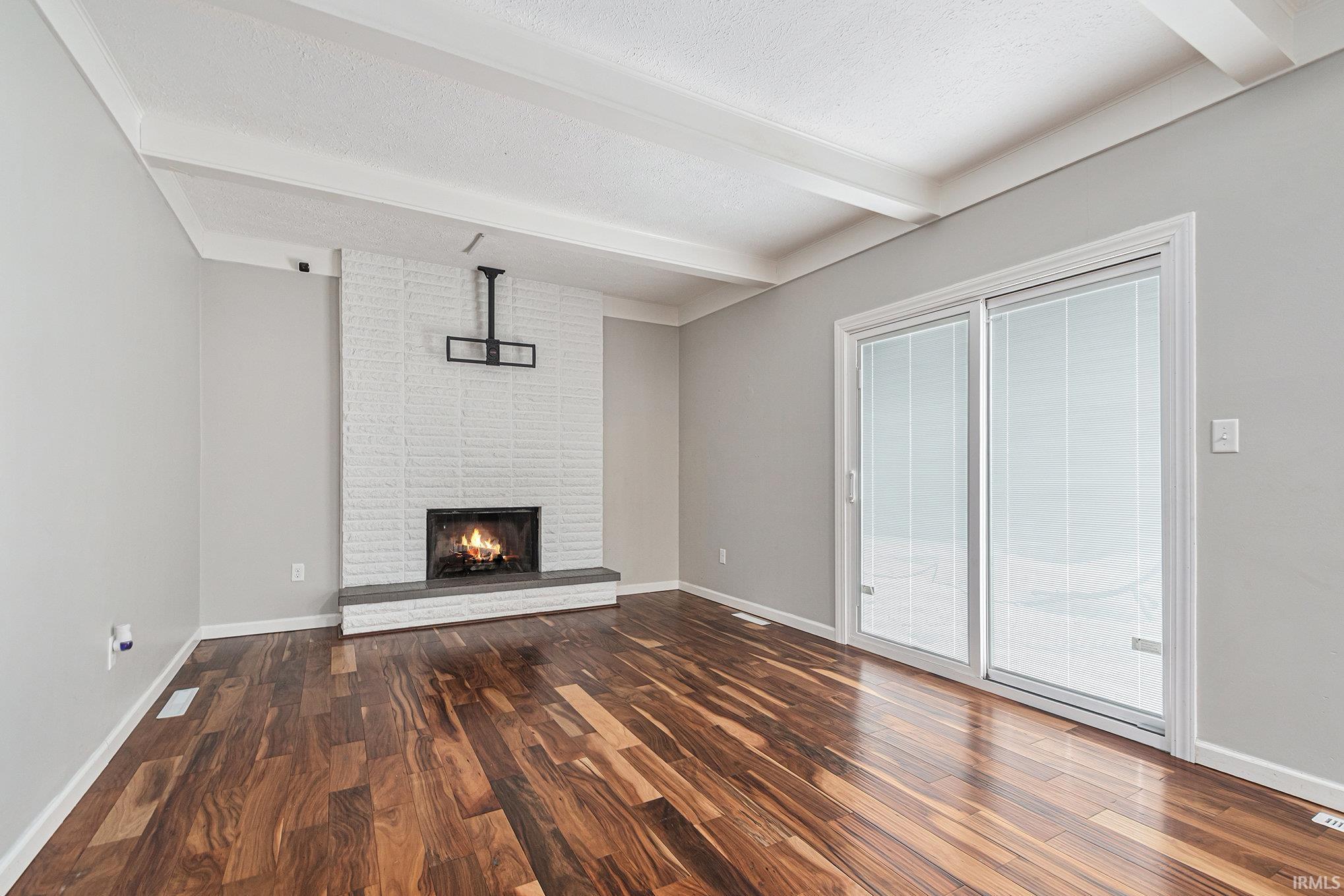 Unfurnished living room featuring beam ceiling, dark wood-style flooring, and a wood fireplace