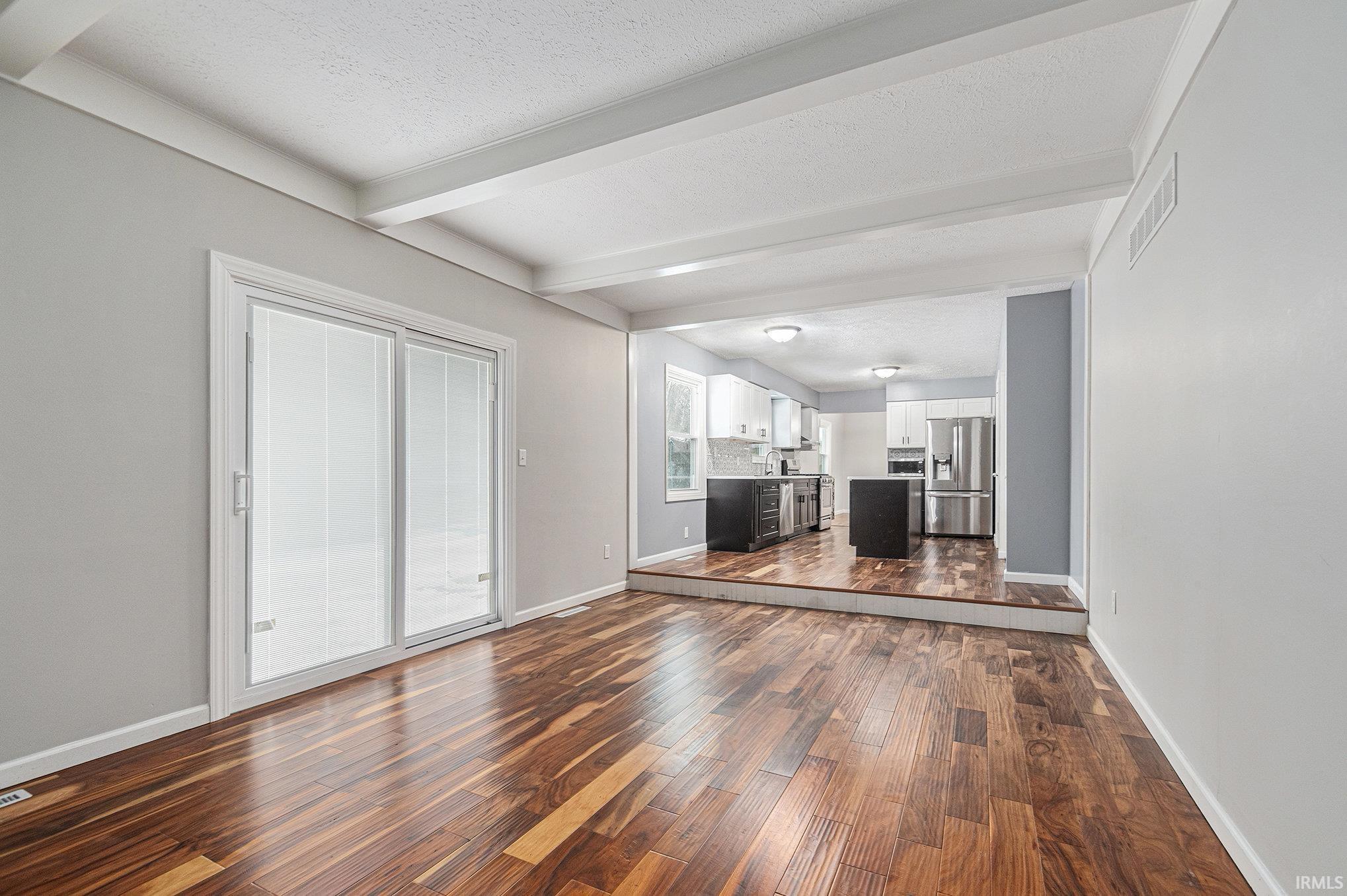 Unfurnished living room featuring beam ceiling, dark wood-style finished floors, and a textured ceiling