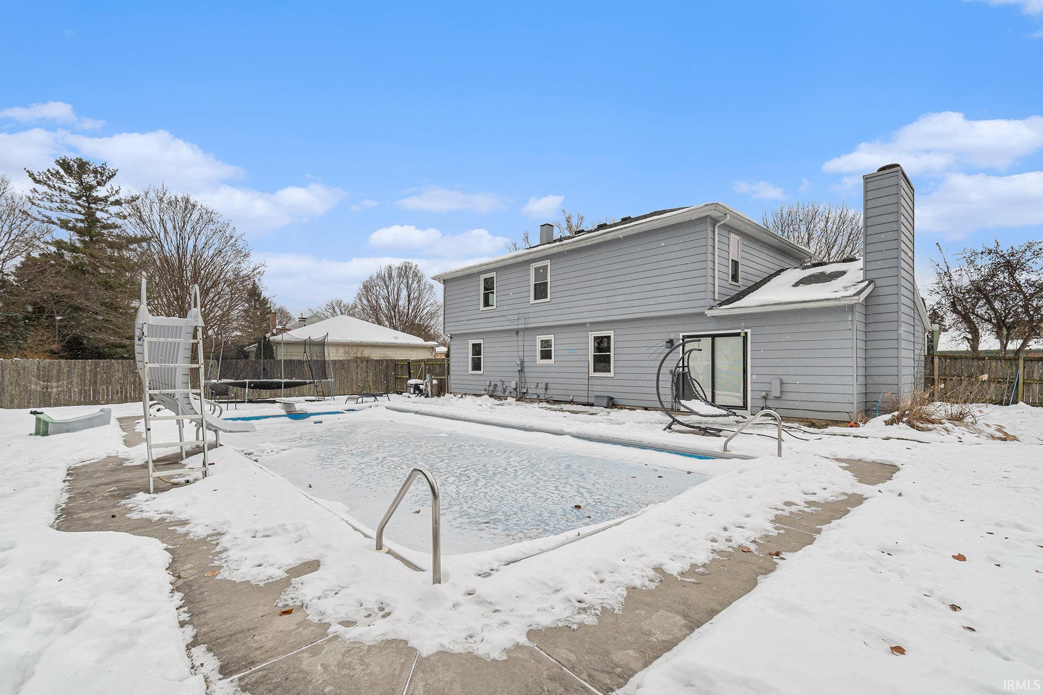 Snow covered back of property with a fenced backyard and a chimney