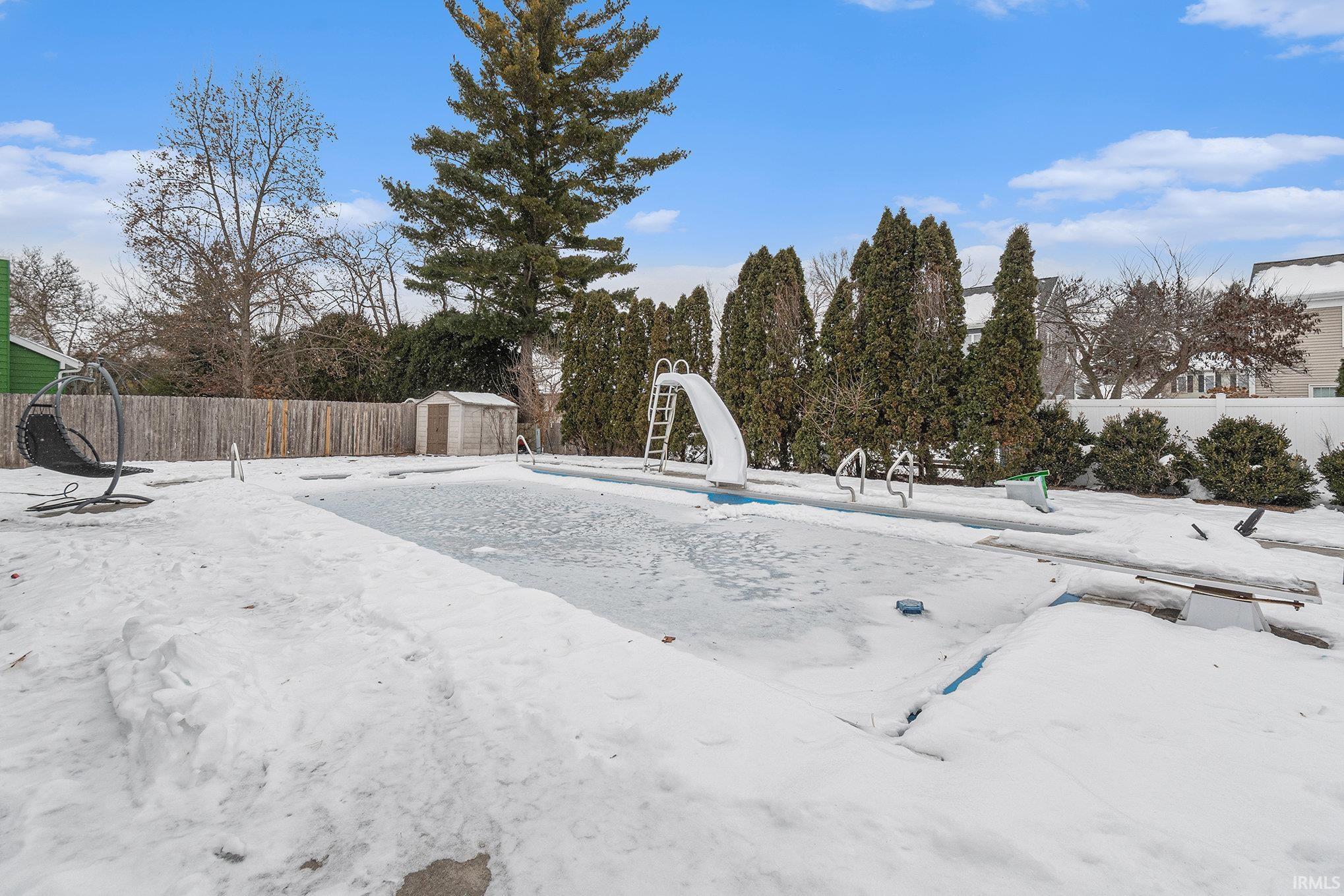 Snowy yard featuring a fenced backyard and a storage unit