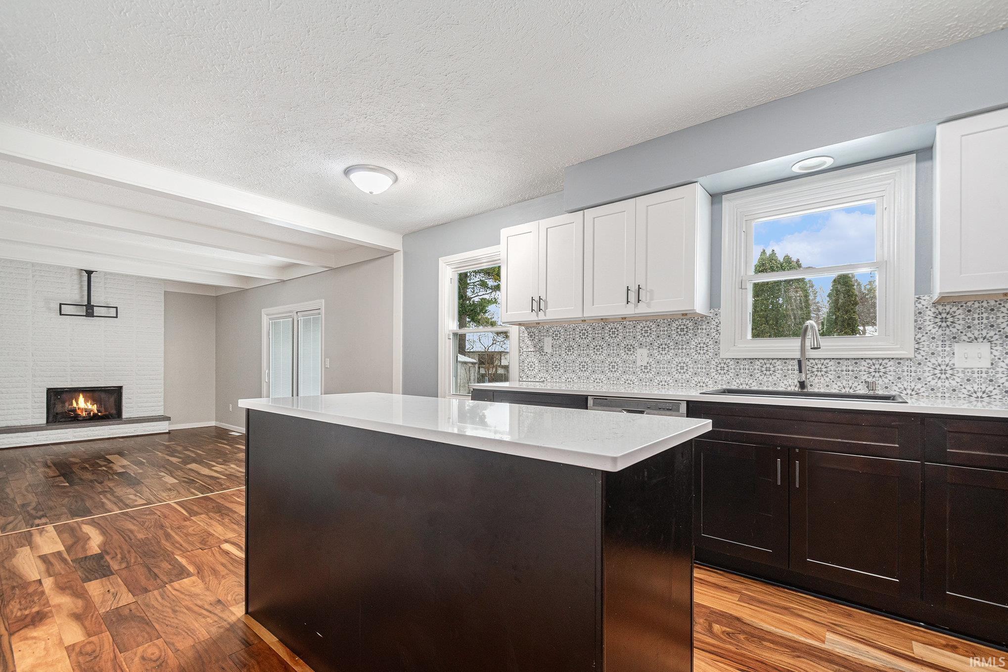 Kitchen featuring a textured ceiling, a center island, light wood finished floors, open floor plan, and decorative backsplash
